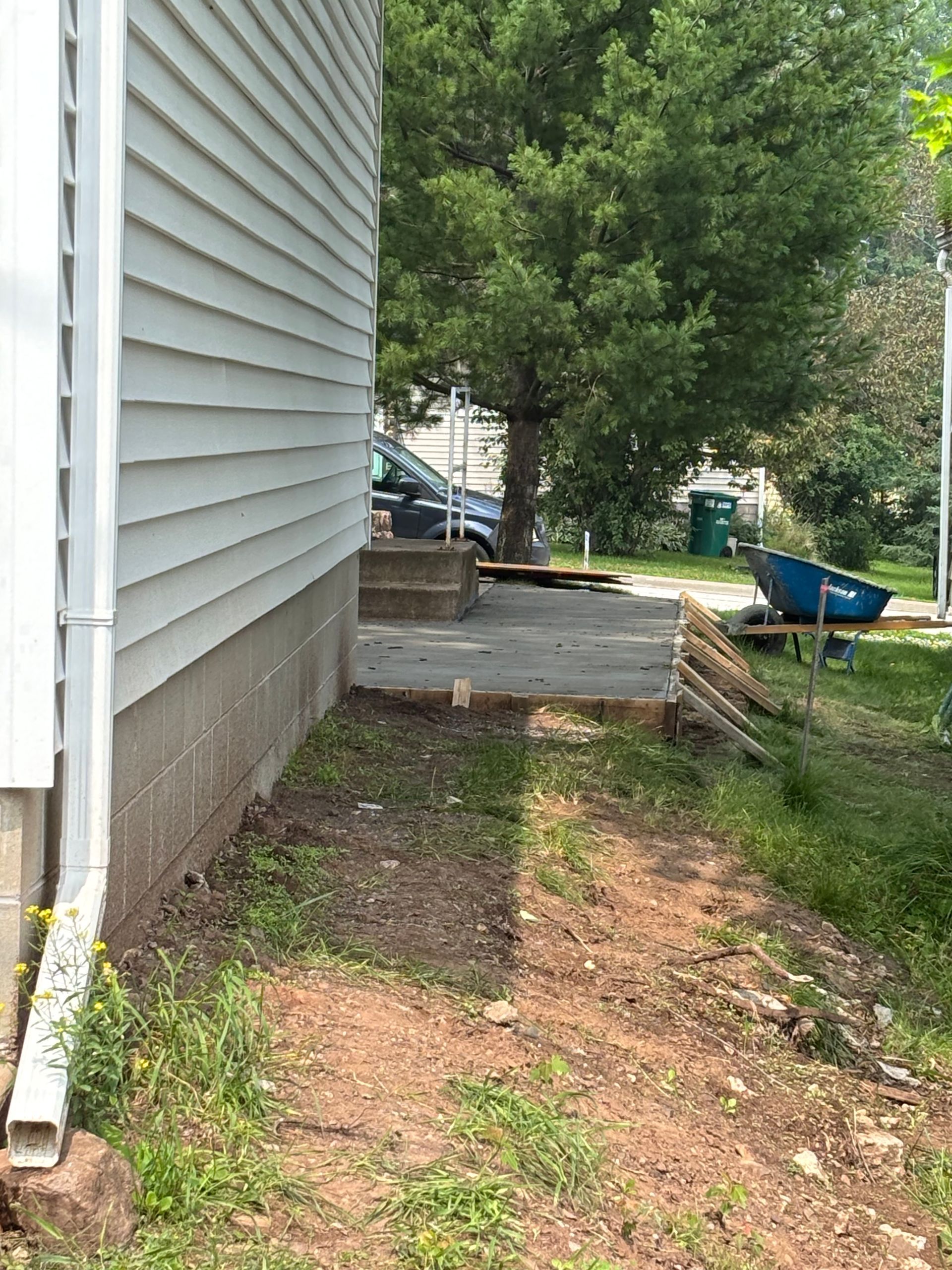 Side view of a house with a concrete walkway leading to a porch and steps. Green grass and a tree are in the background.