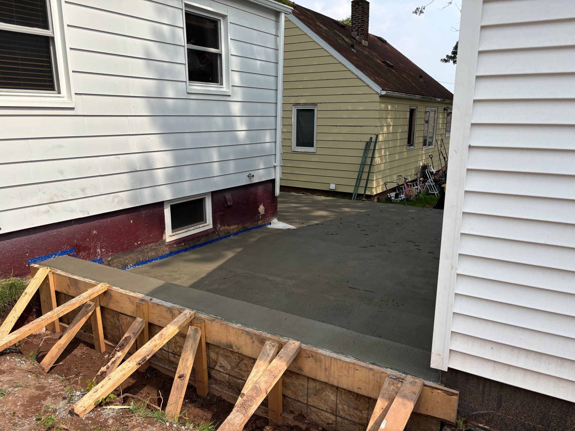 Newly poured concrete patio between two houses, with wooden formwork in the foreground.