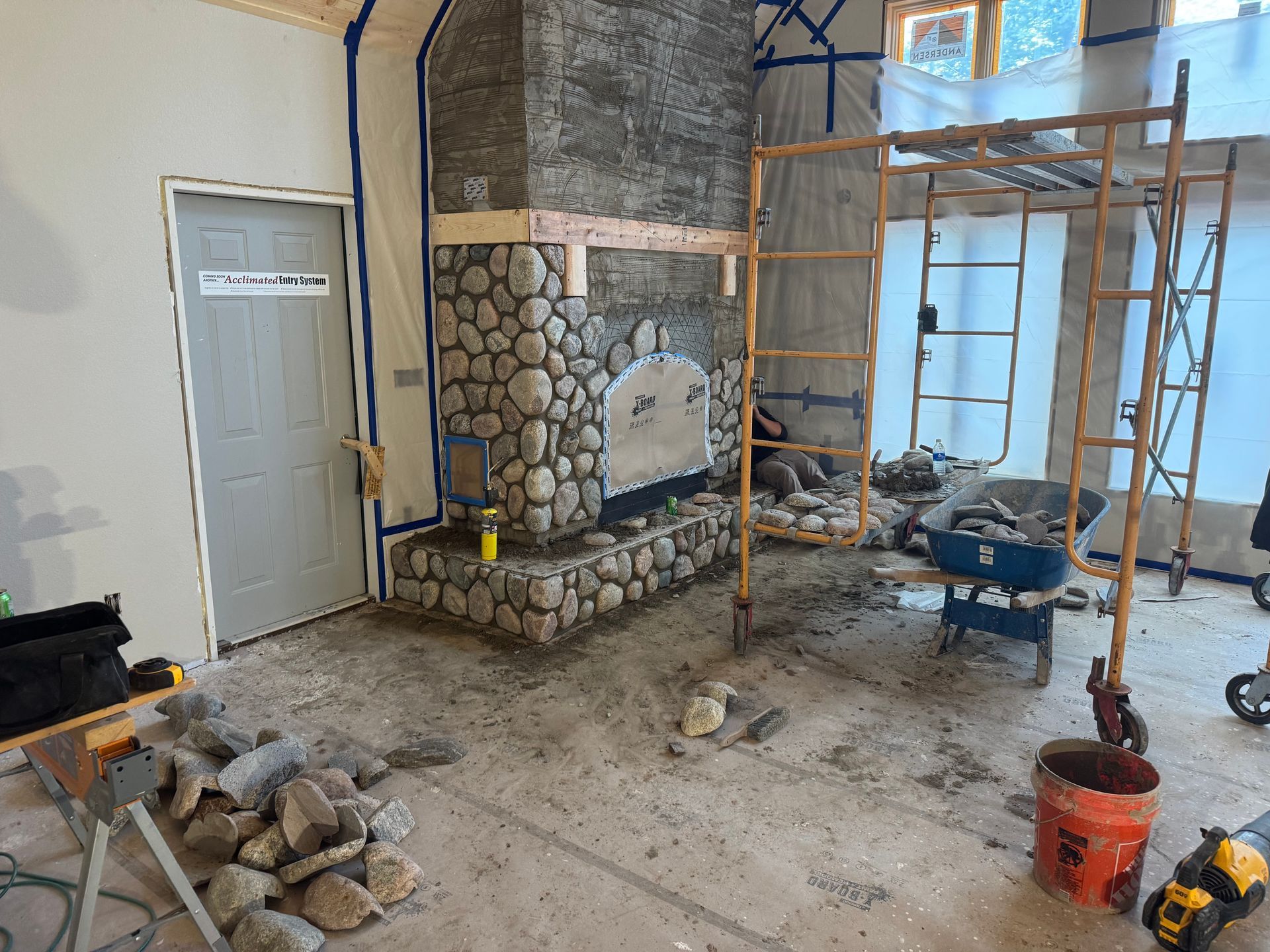 Stone fireplace under construction in a room, with scaffolding and protective sheeting.