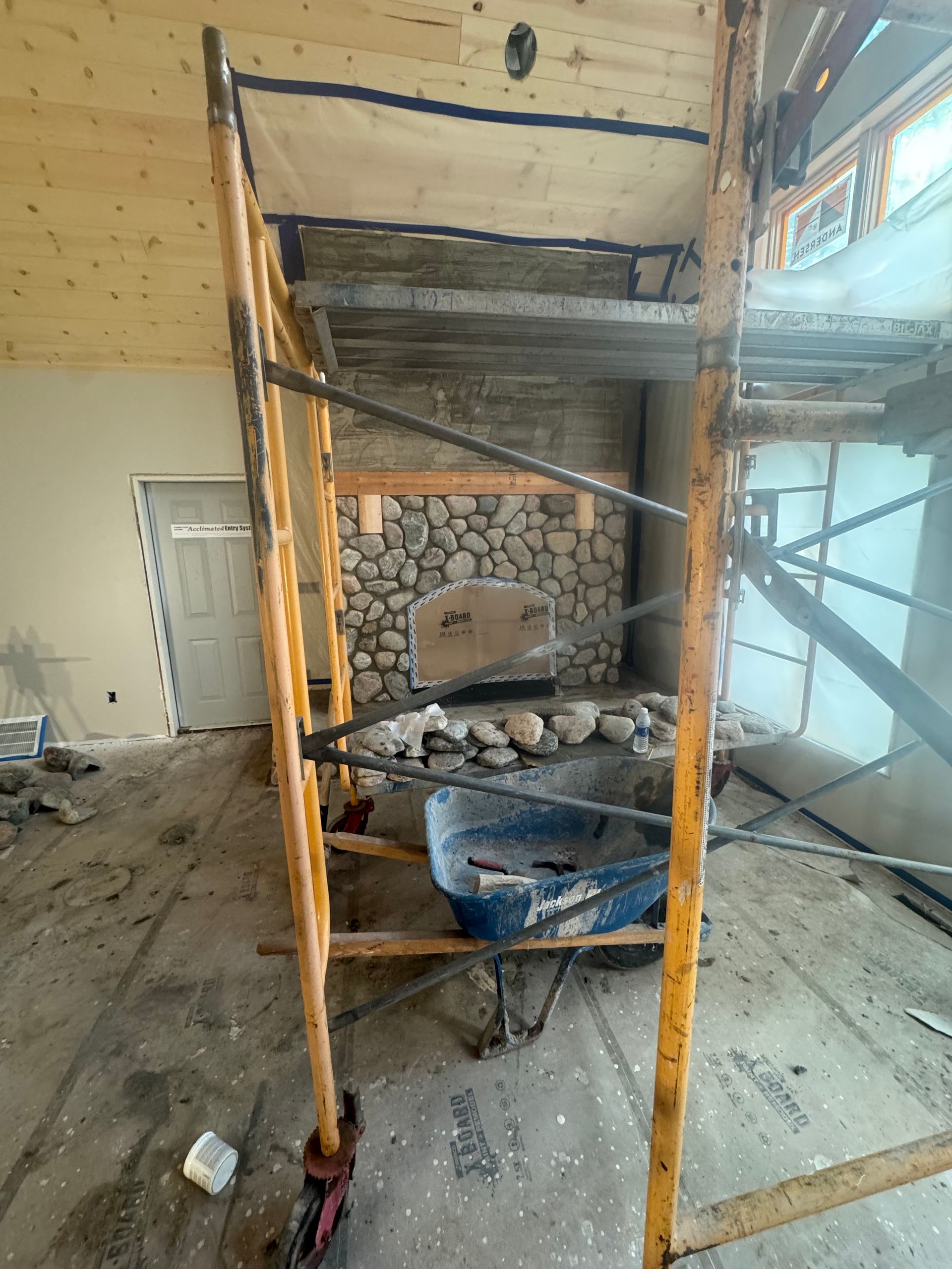 Construction site: rock fireplace under construction with scaffolding. Interior view, wooden ceiling and a door.