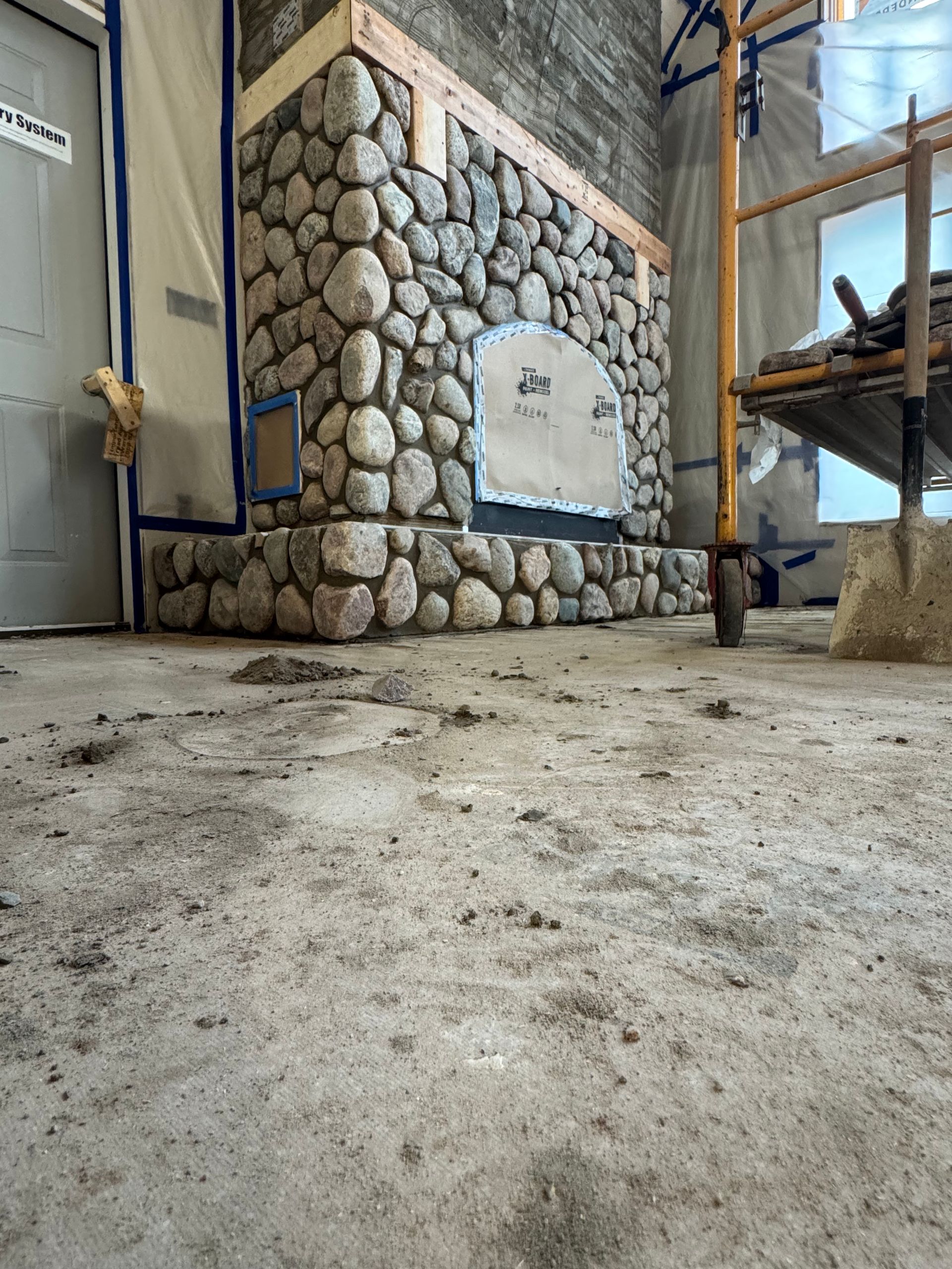 Stone fireplace under construction in a room, with scaffolding and protective covering.