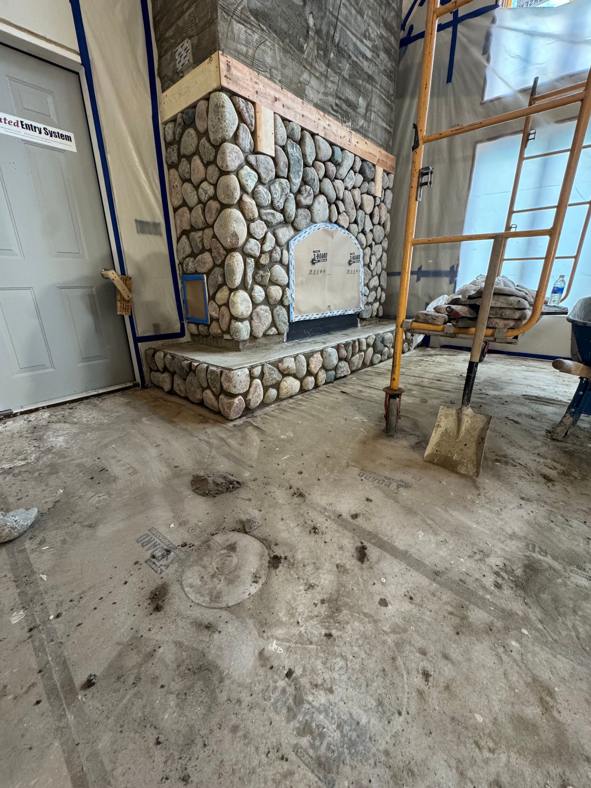 Stone fireplace under construction with a concrete hearth. Scaffolding and tools present in the room.