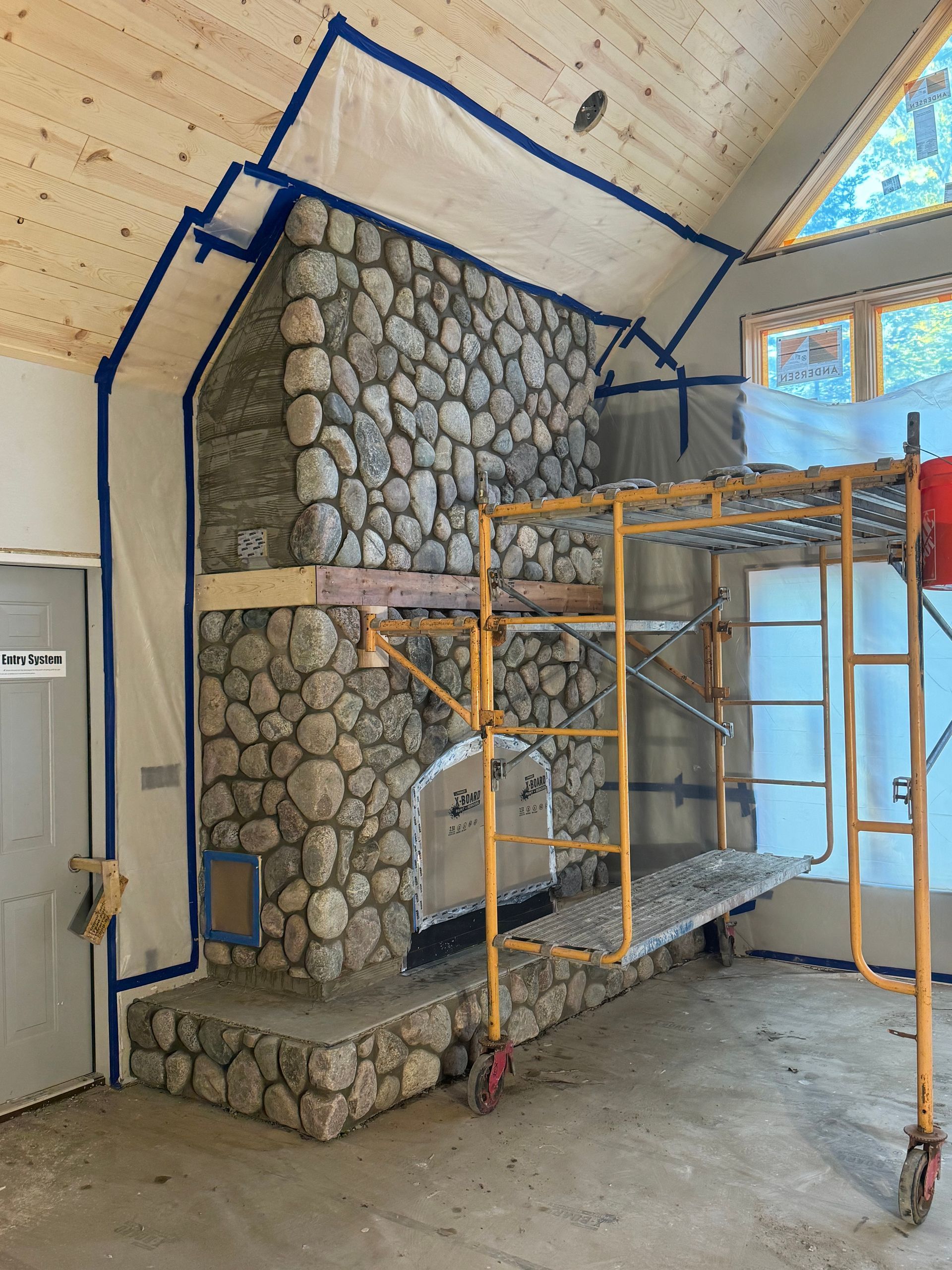 Stone fireplace under construction with scaffolding and protective sheeting.
