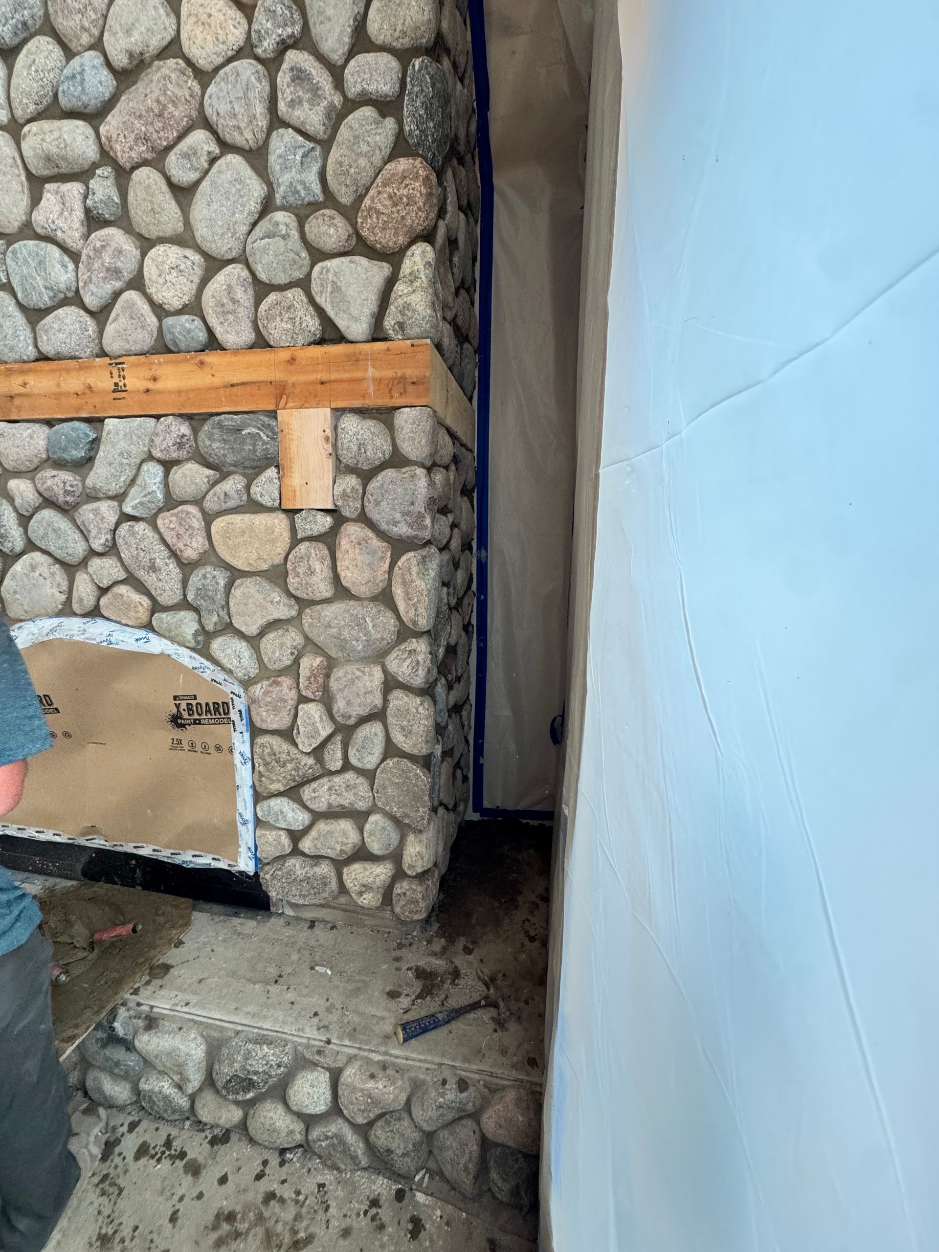Stone fireplace under construction next to a wall. Tape and protective sheeting visible.