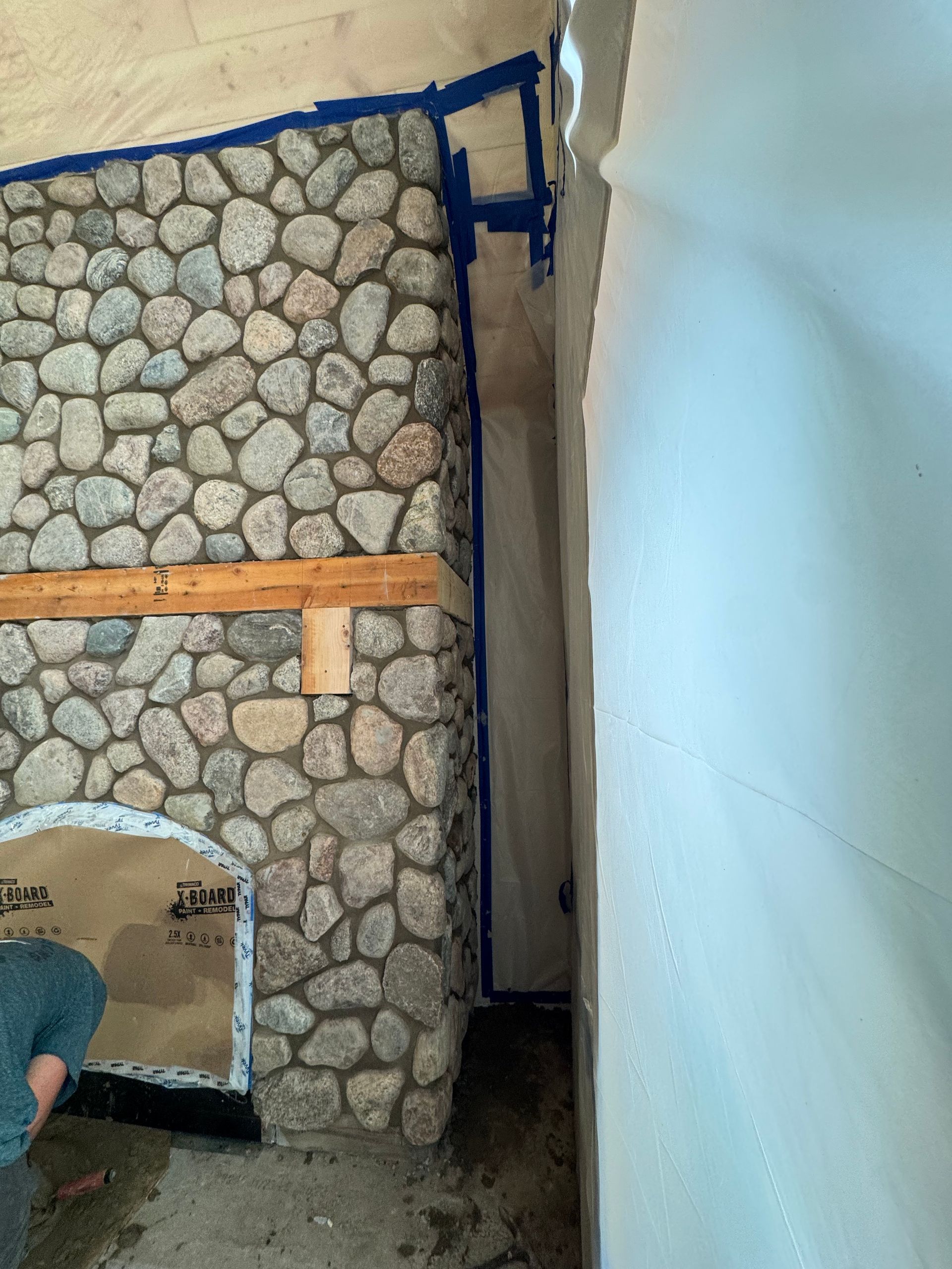 Stone fireplace under construction with blue tape and plastic sheeting.