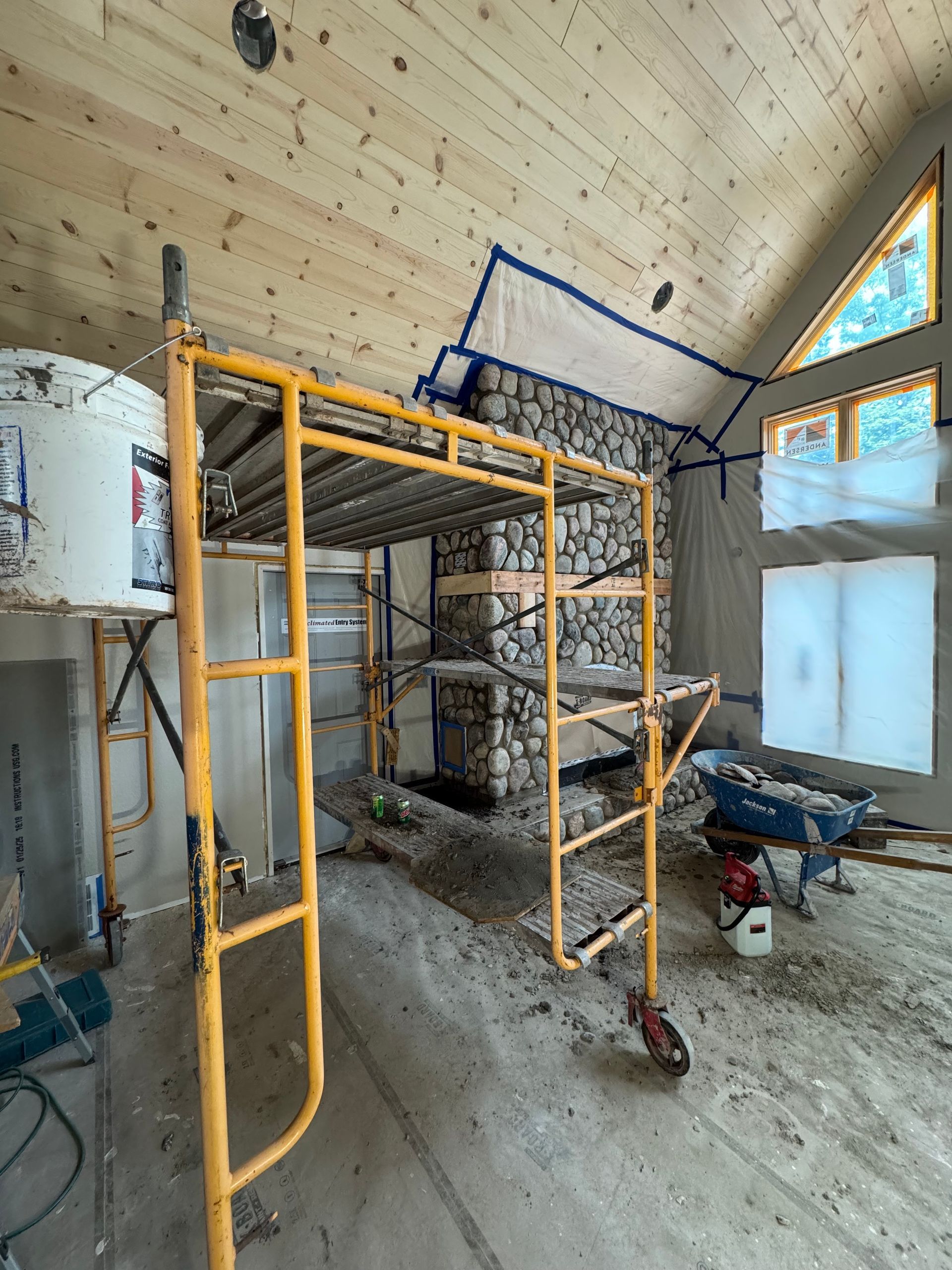 Interior construction site with stone fireplace, scaffolding, and unfinished walls.