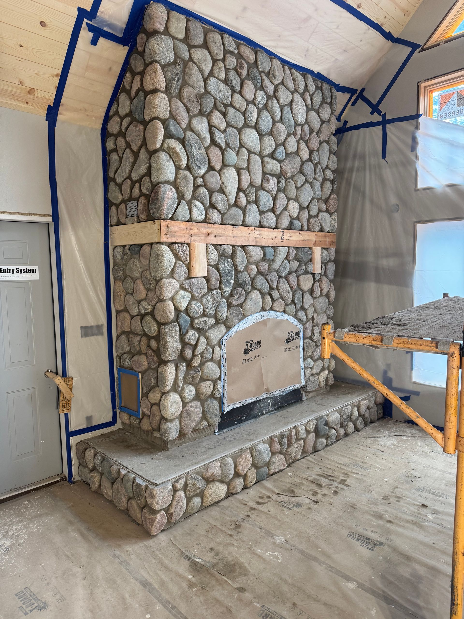 Stone fireplace under construction in a room. Blue tape protects adjacent surfaces.