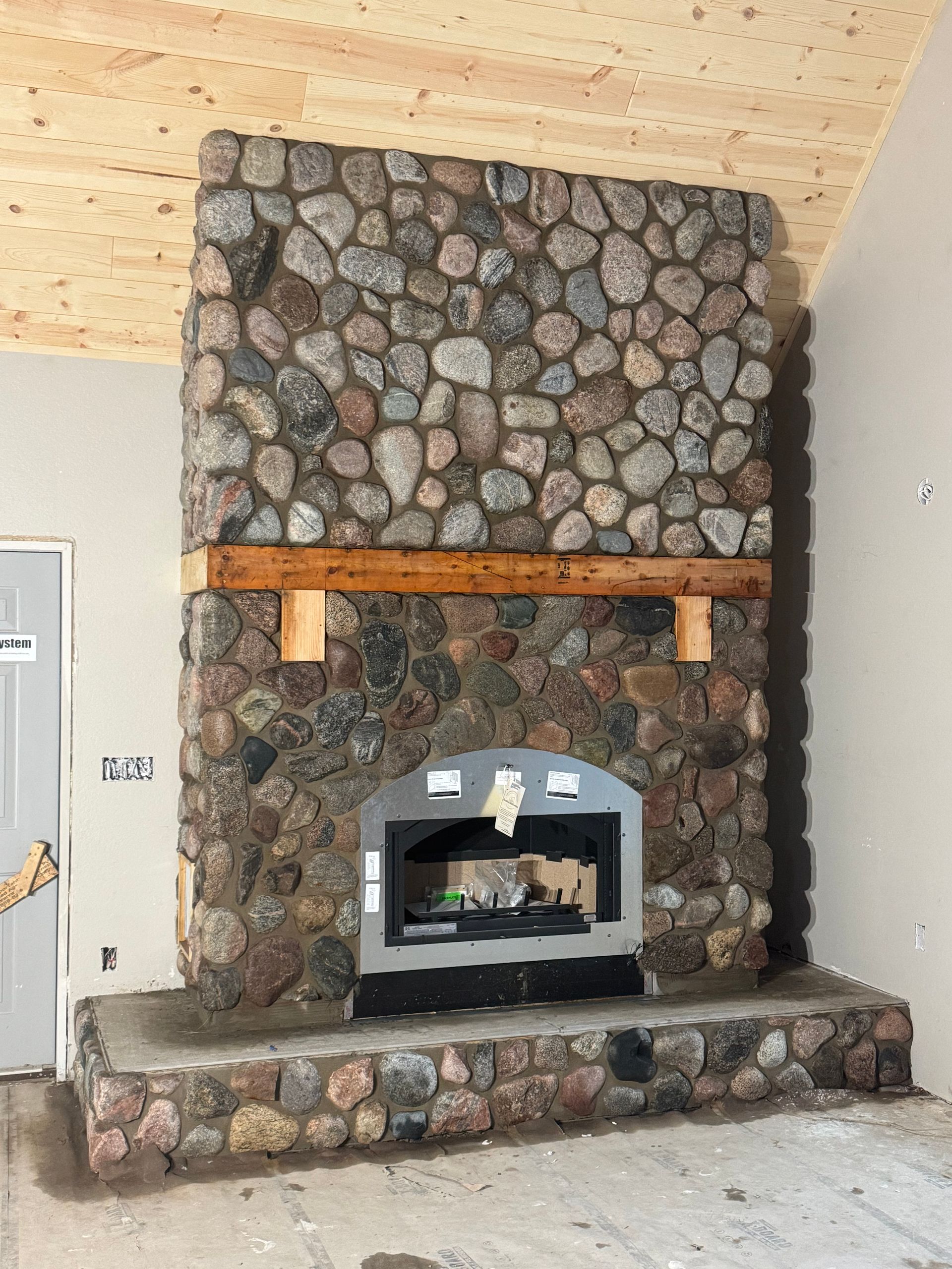 Stone fireplace with wooden mantle and inset silver firebox, built-in a room with exposed wood ceiling.