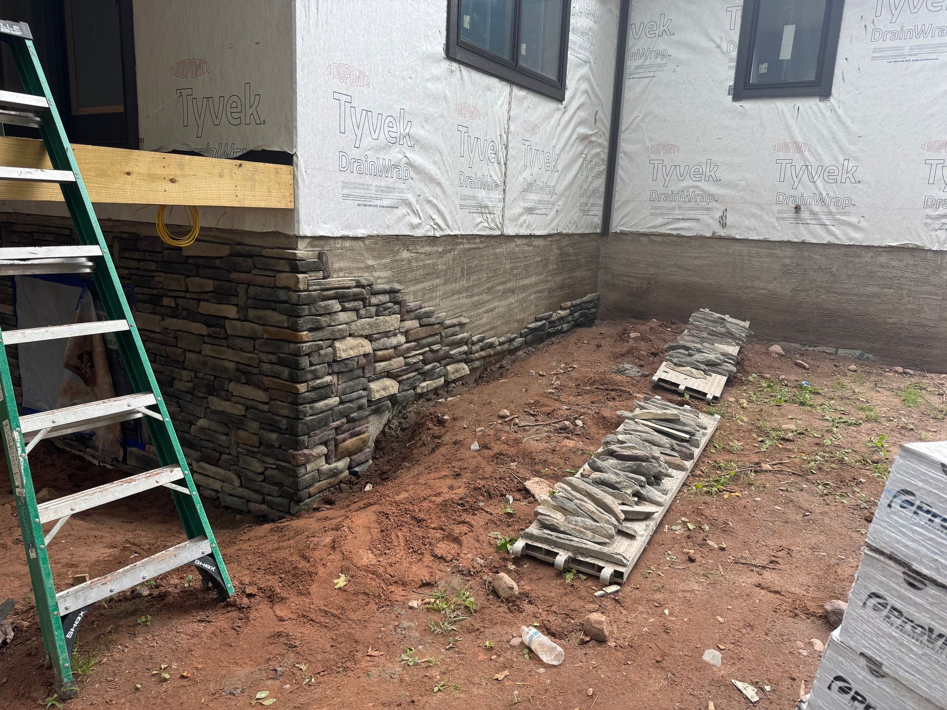 Construction of stone veneer on a house, with a ladder and building materials.