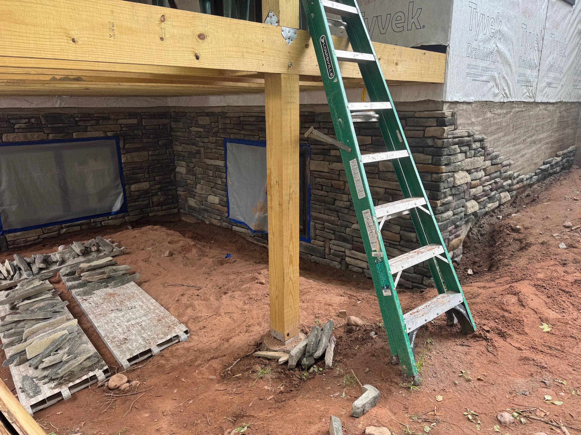 Construction site with stone veneer being installed on a building's exterior. A ladder leans against the structure.
