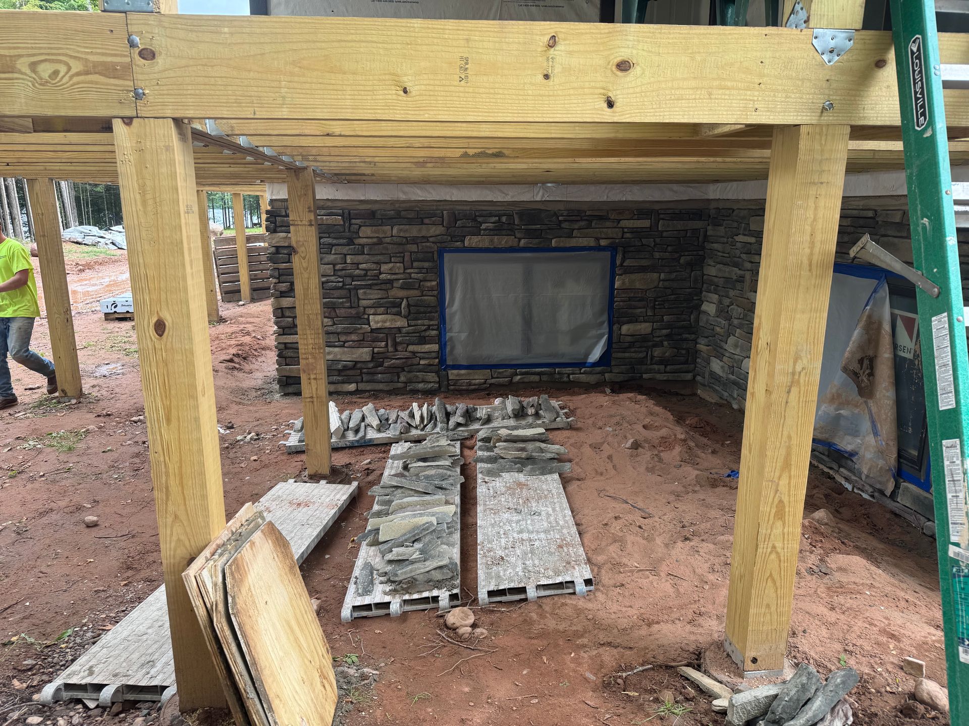 Construction of an outdoor space with stone wall, wooden beams and posts, and scattered paving stones.