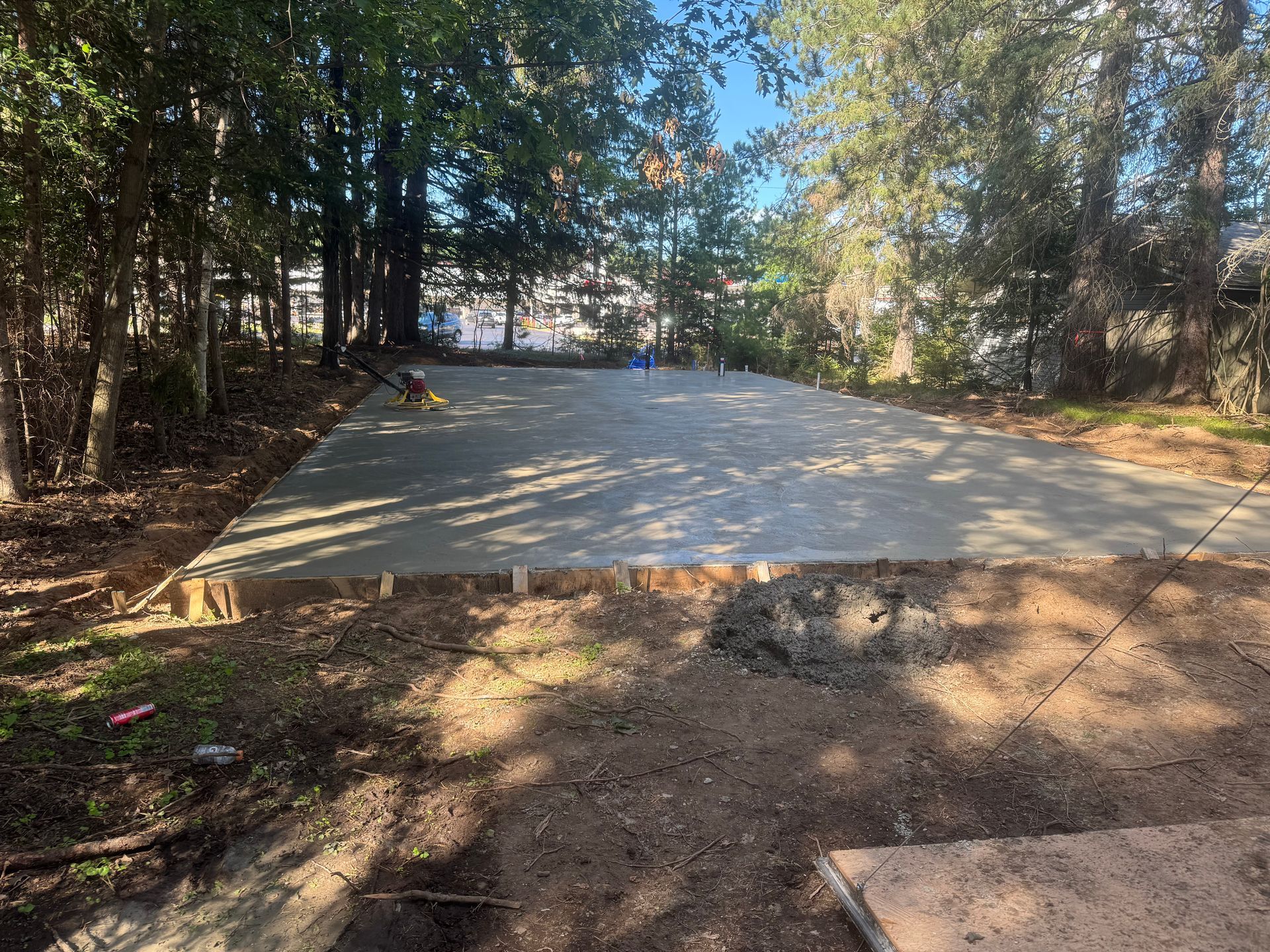 Newly poured concrete slab in a wooded backyard.