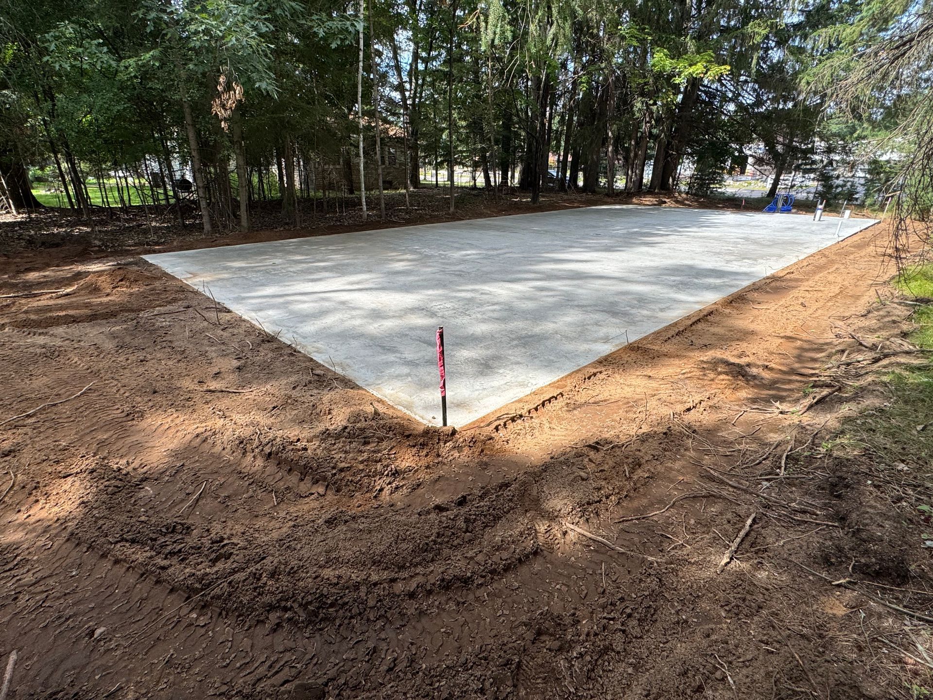 Gravel-covered, triangular area prepared for construction, surrounded by dirt and trees in a backyard setting.