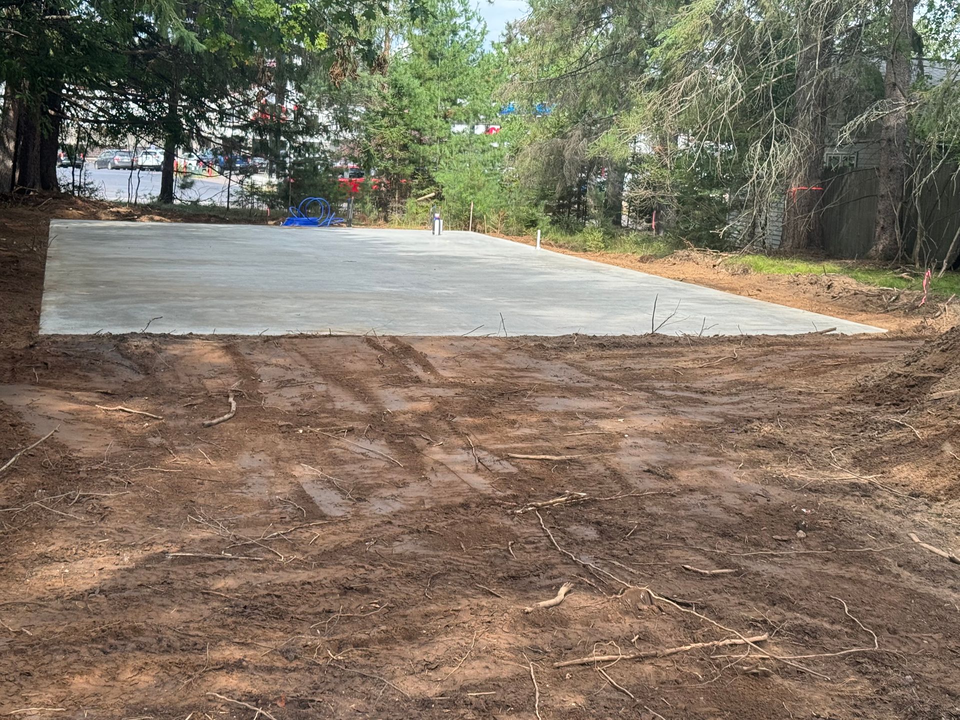 A newly poured concrete slab surrounded by dirt and trees, likely for a building foundation.