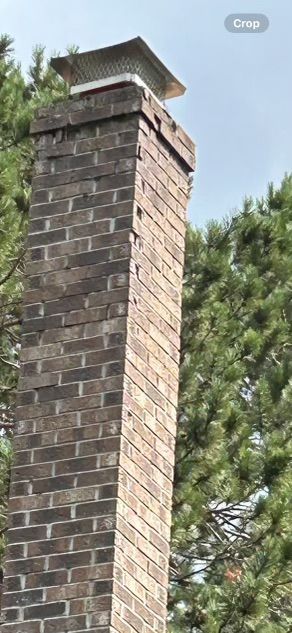 Brick chimney with a metal cap. Green trees and blue sky are visible.