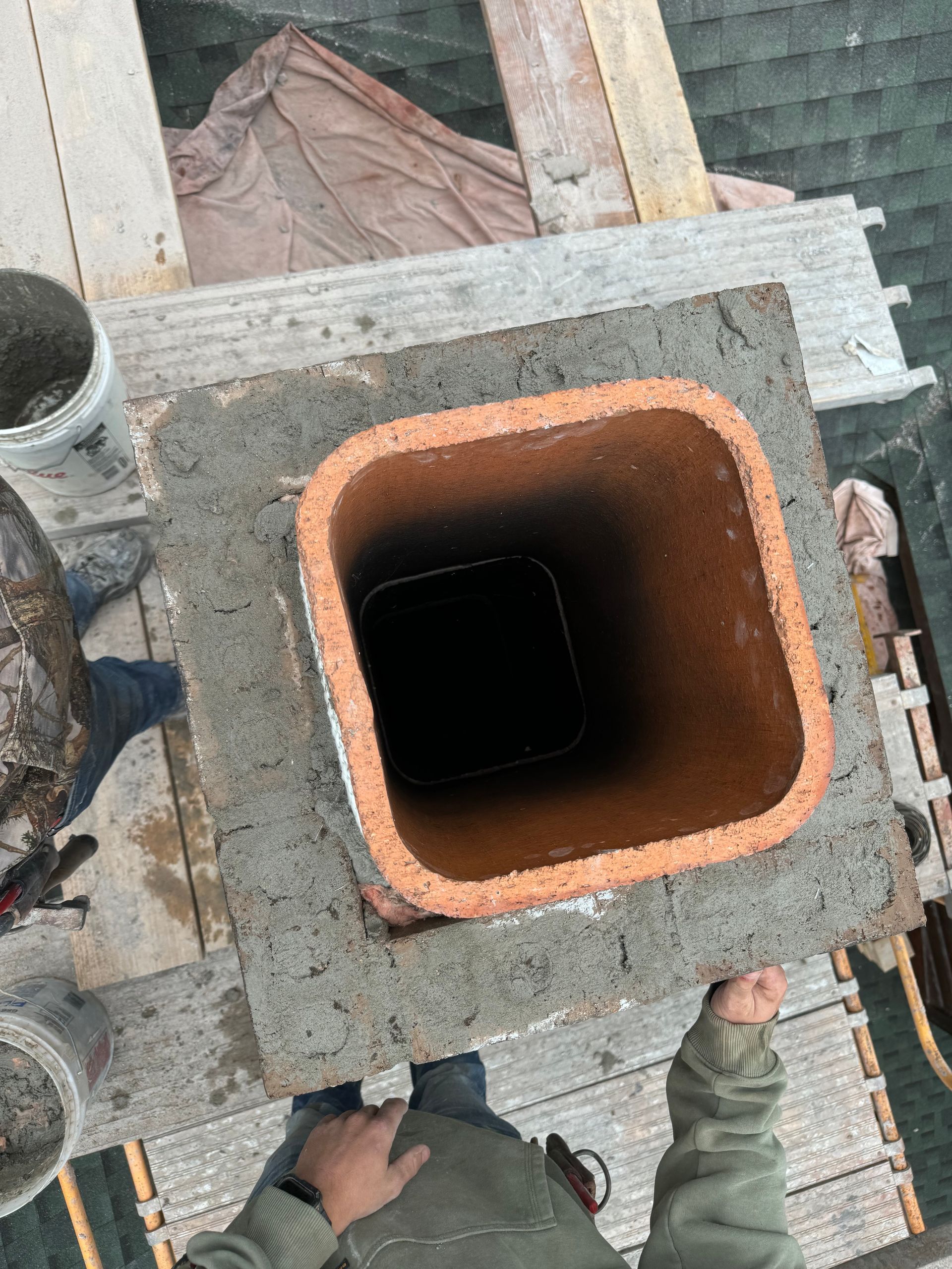 Overhead view of a chimney interior. A person’s hands are visible. Cement base with a square, dark flue.