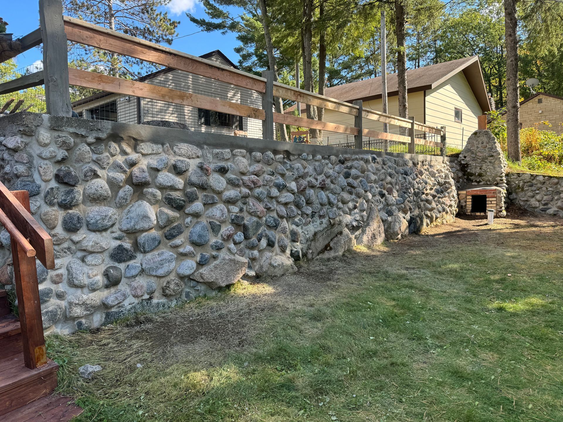 Stone wall with wooden fence and building behind, on a grassy area.