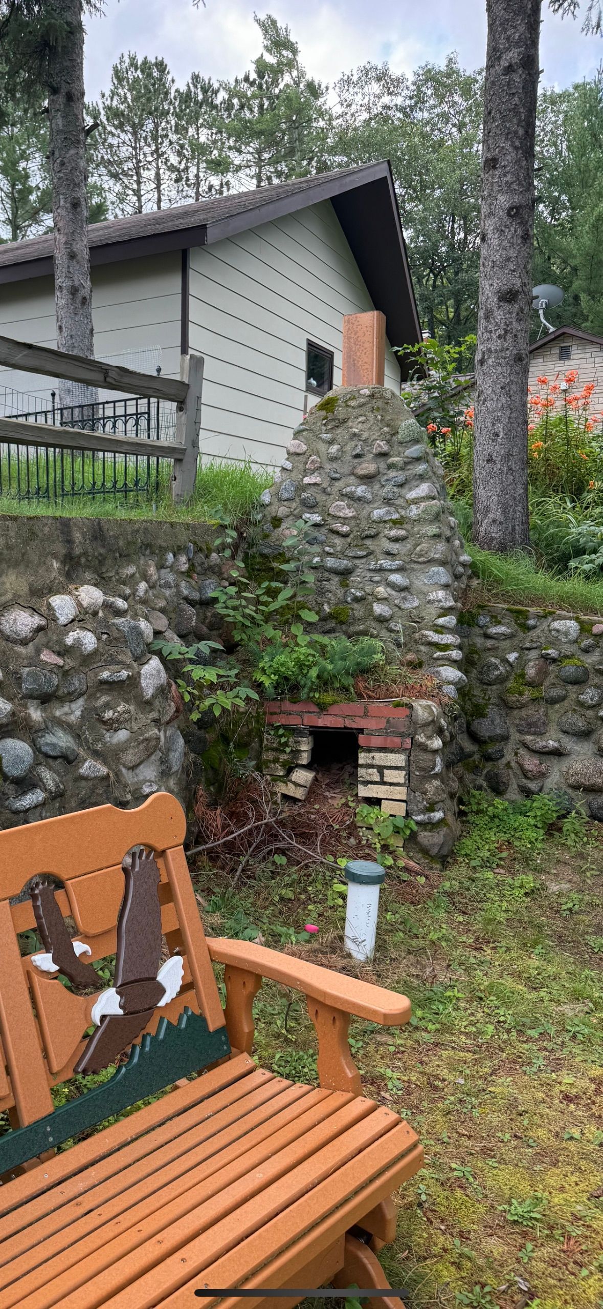 A stone outdoor fireplace next to a cabin, with a wooden bench in the foreground.
