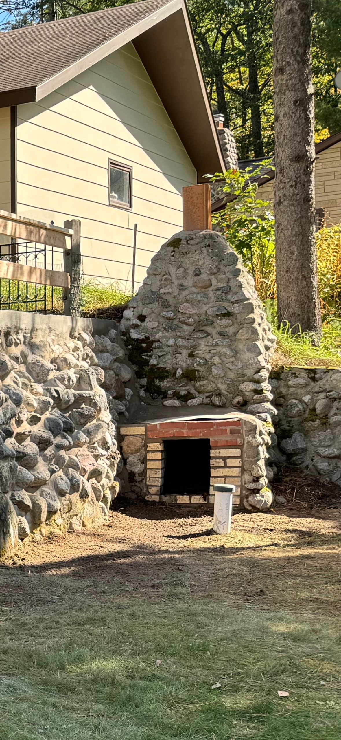 Stone and brick outdoor fireplace in a yard, with house and trees in the background.