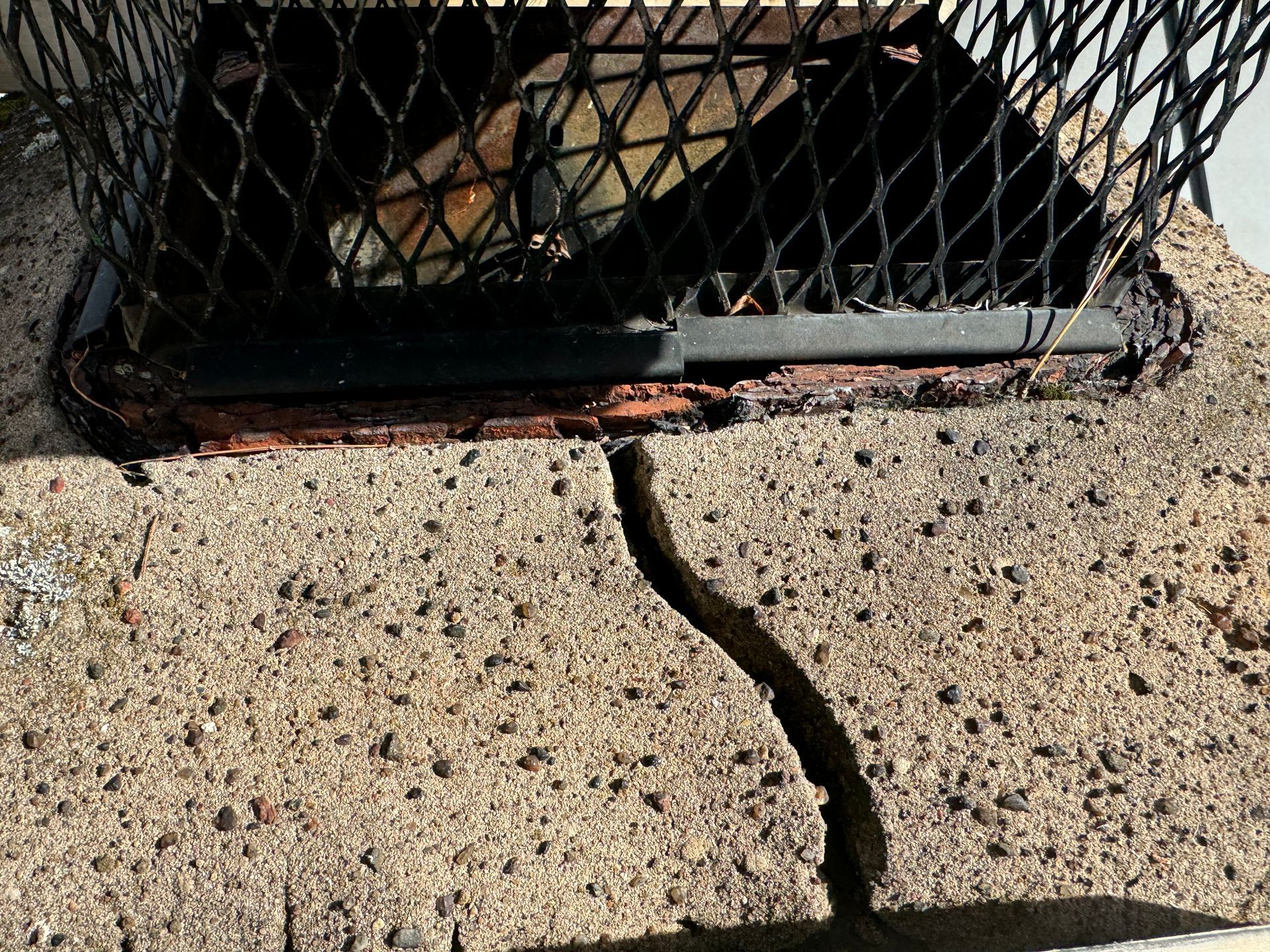 Close-up of a concrete structure with a metal mesh cover and a prominent vertical crack.