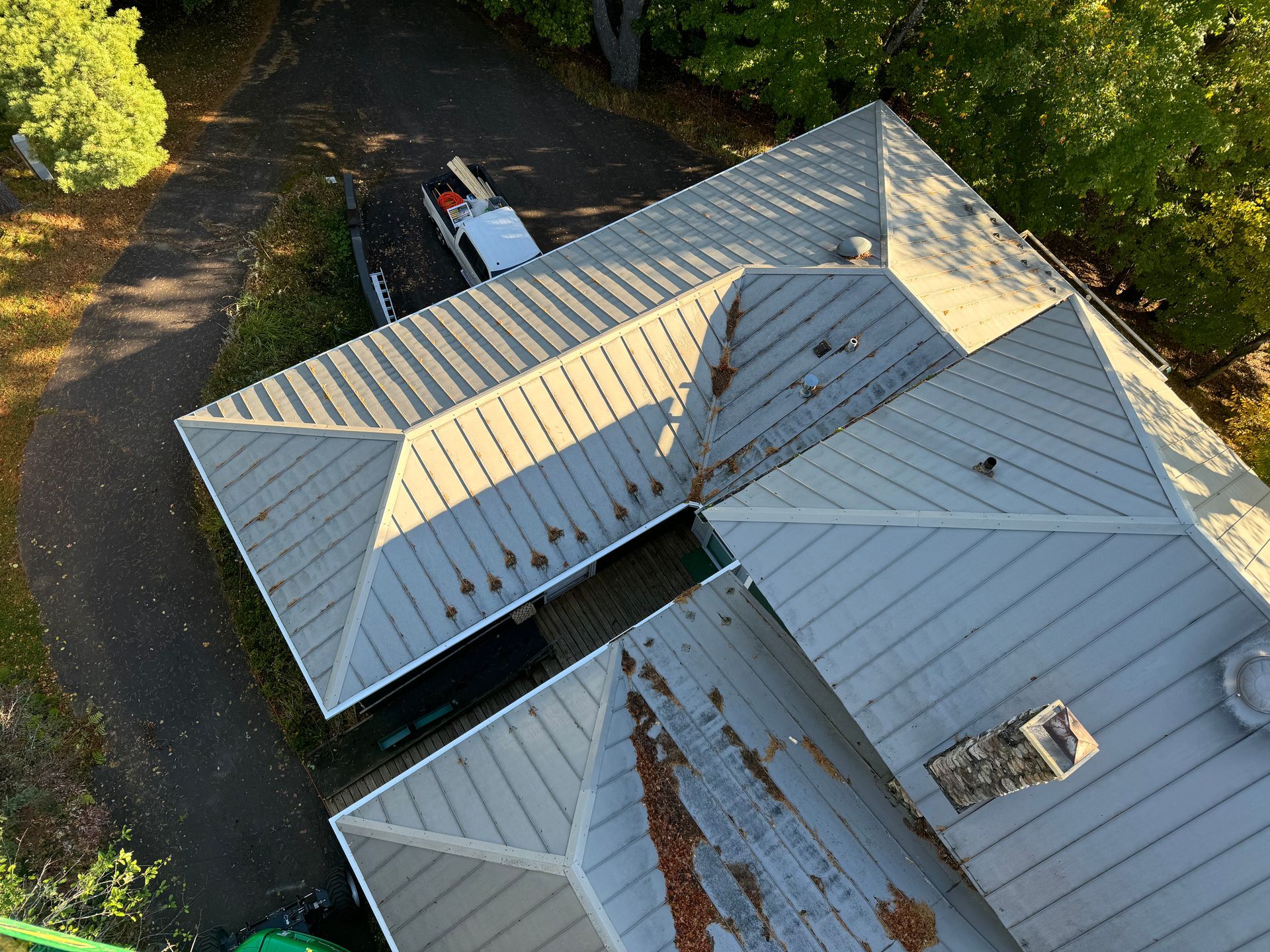 Overhead view of a gray metal roof, possibly residential, with some debris and a truck parked beside it.