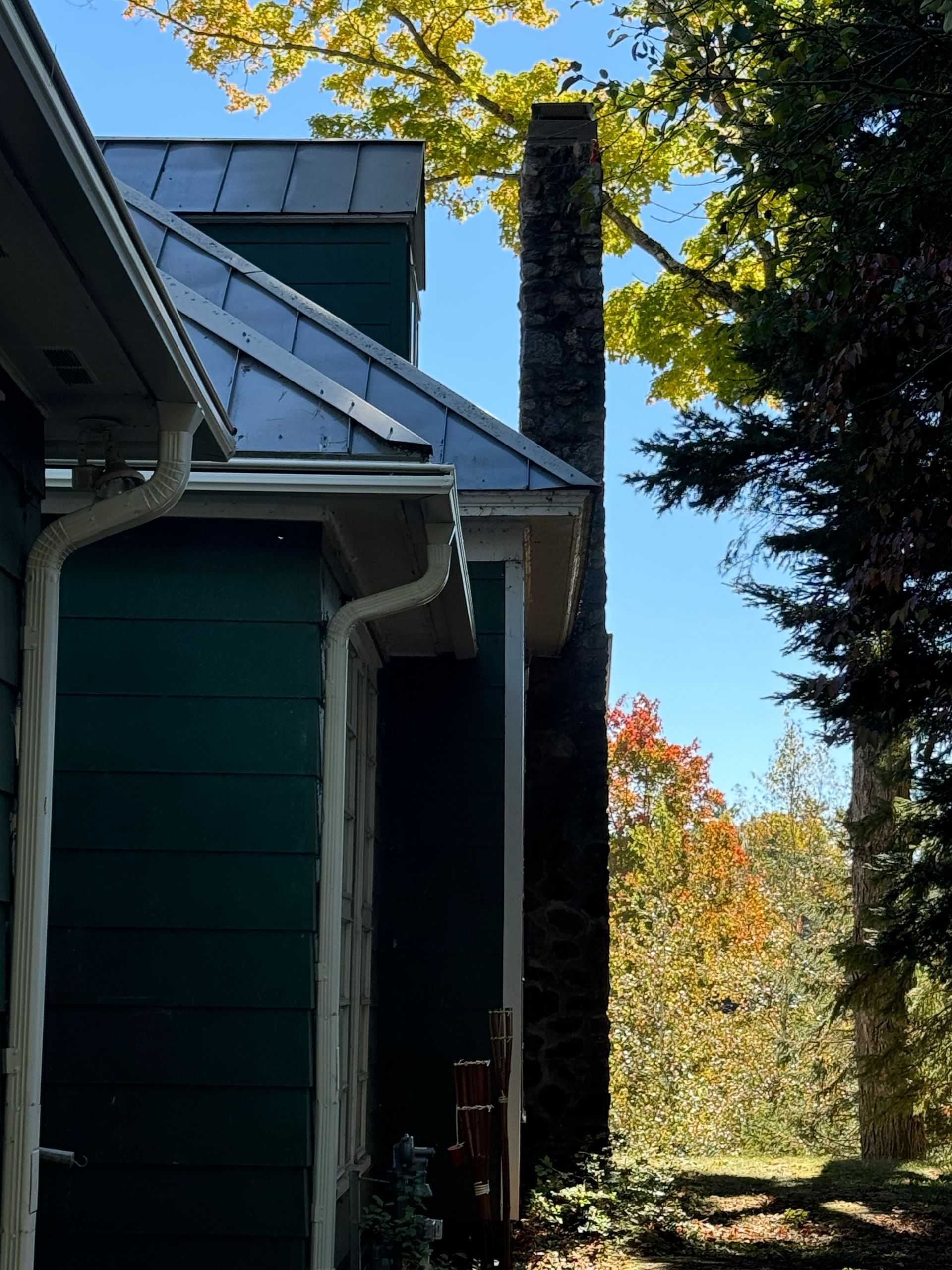 Green house with a chimney against blue sky and fall foliage.