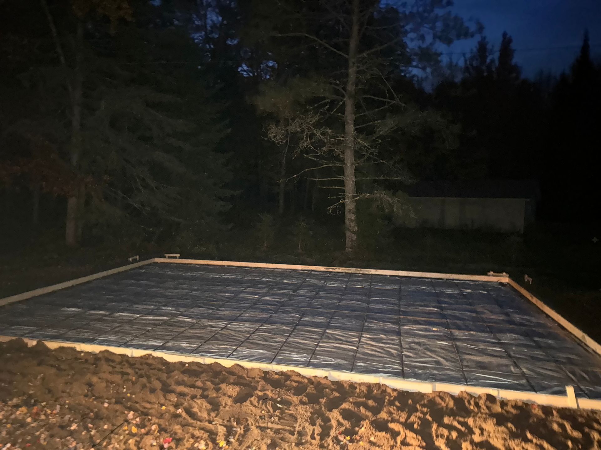 Night shot of a prepared square concrete slab form with mesh in a wooded area.