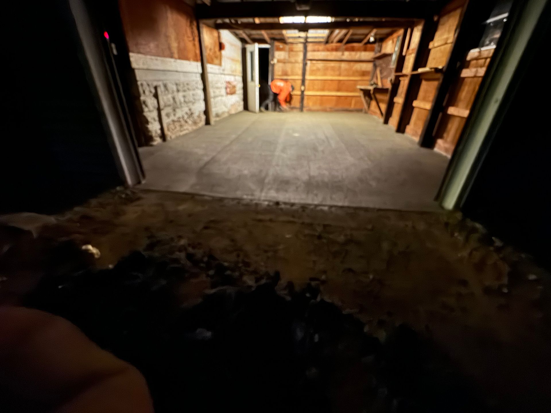 Dark garage interior, new concrete floor, open doorway with dirt and debris in foreground.