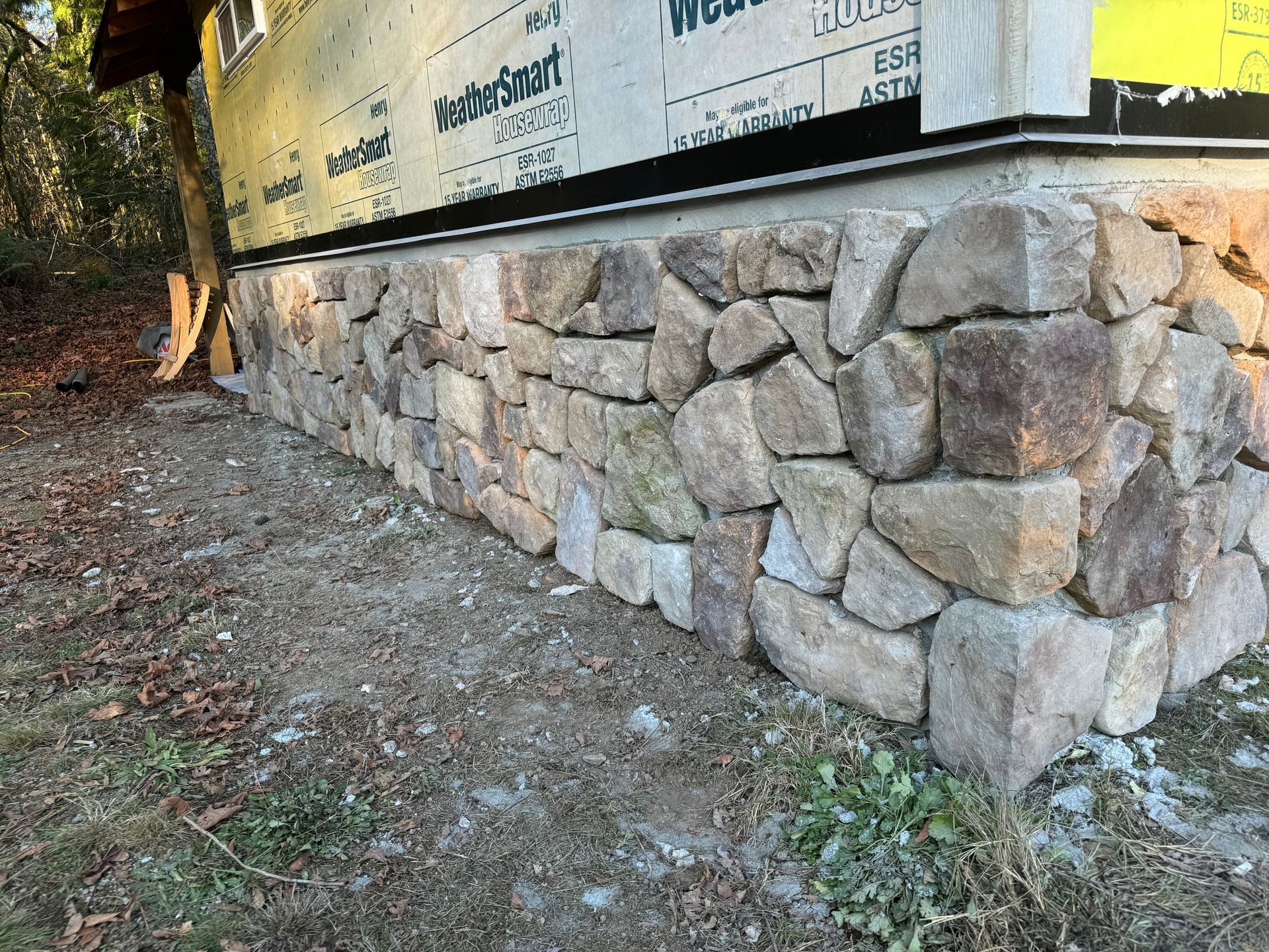 Stone foundation supporting a building's exterior wall. The foundation is made of irregularly shaped, light-colored stones.