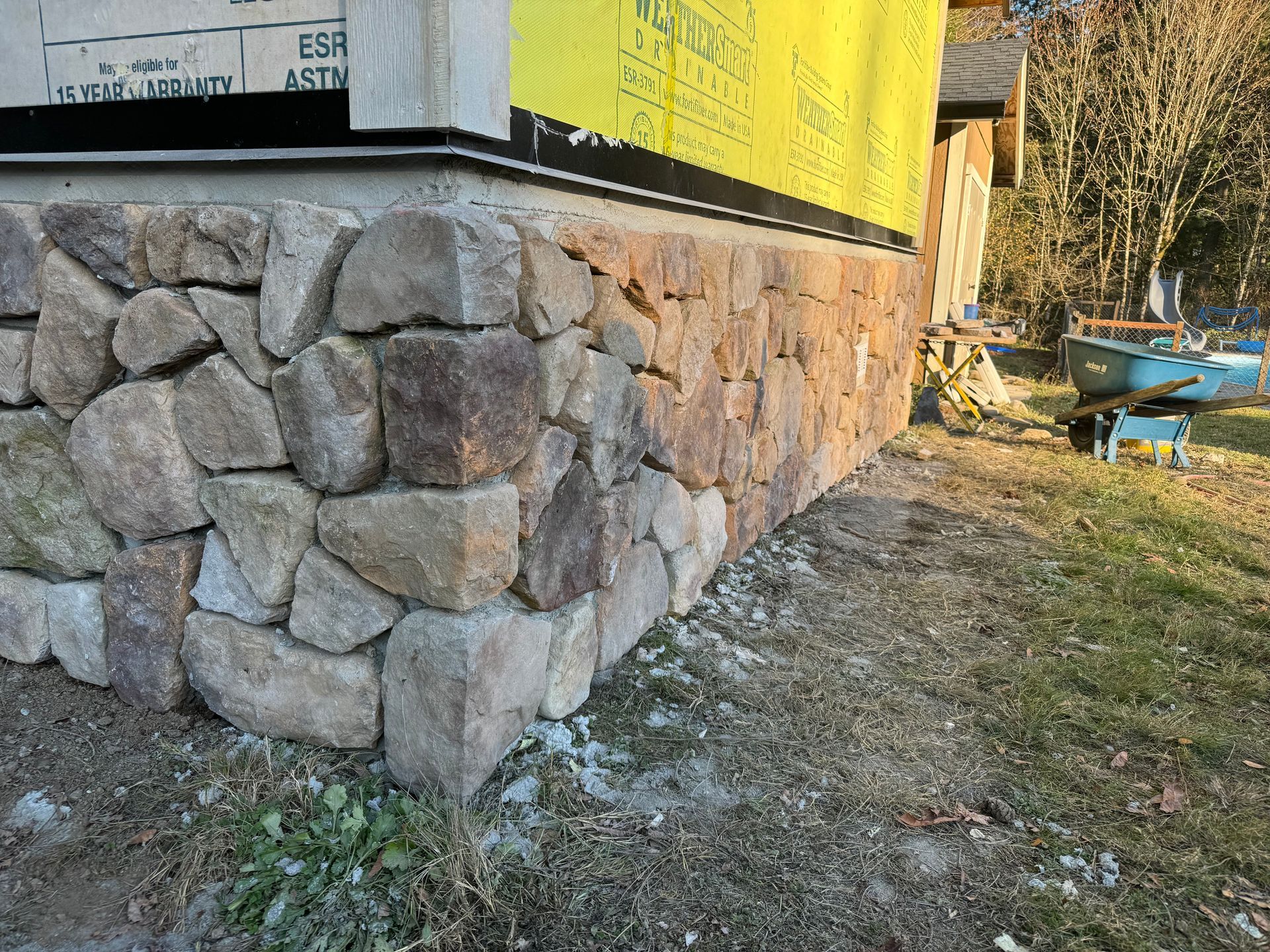 Stone foundation of a building under construction, with exposed wood framing and sheathing.