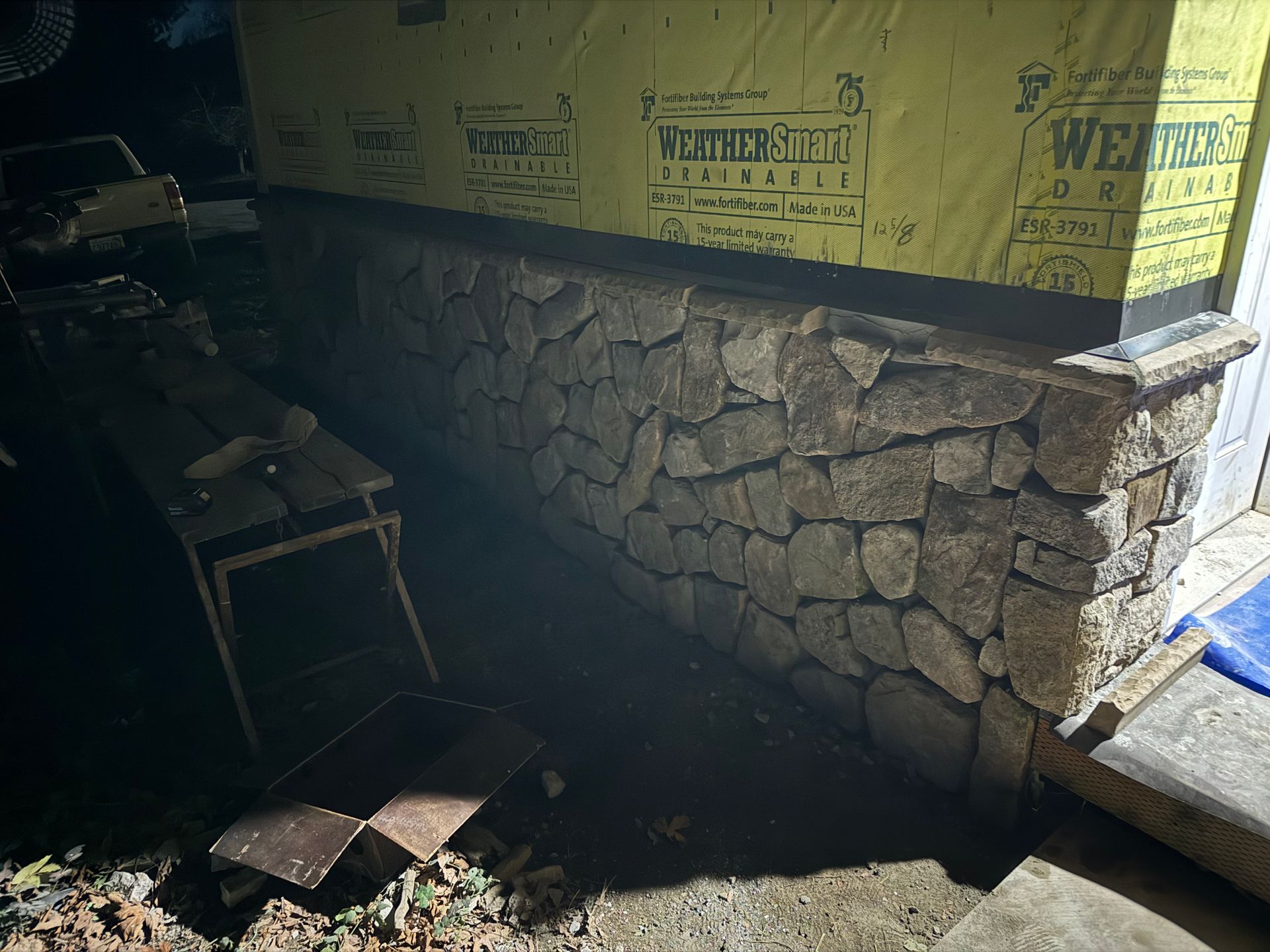Stone veneer on a building's foundation wall, with yellow sheathing above. Dark surroundings.