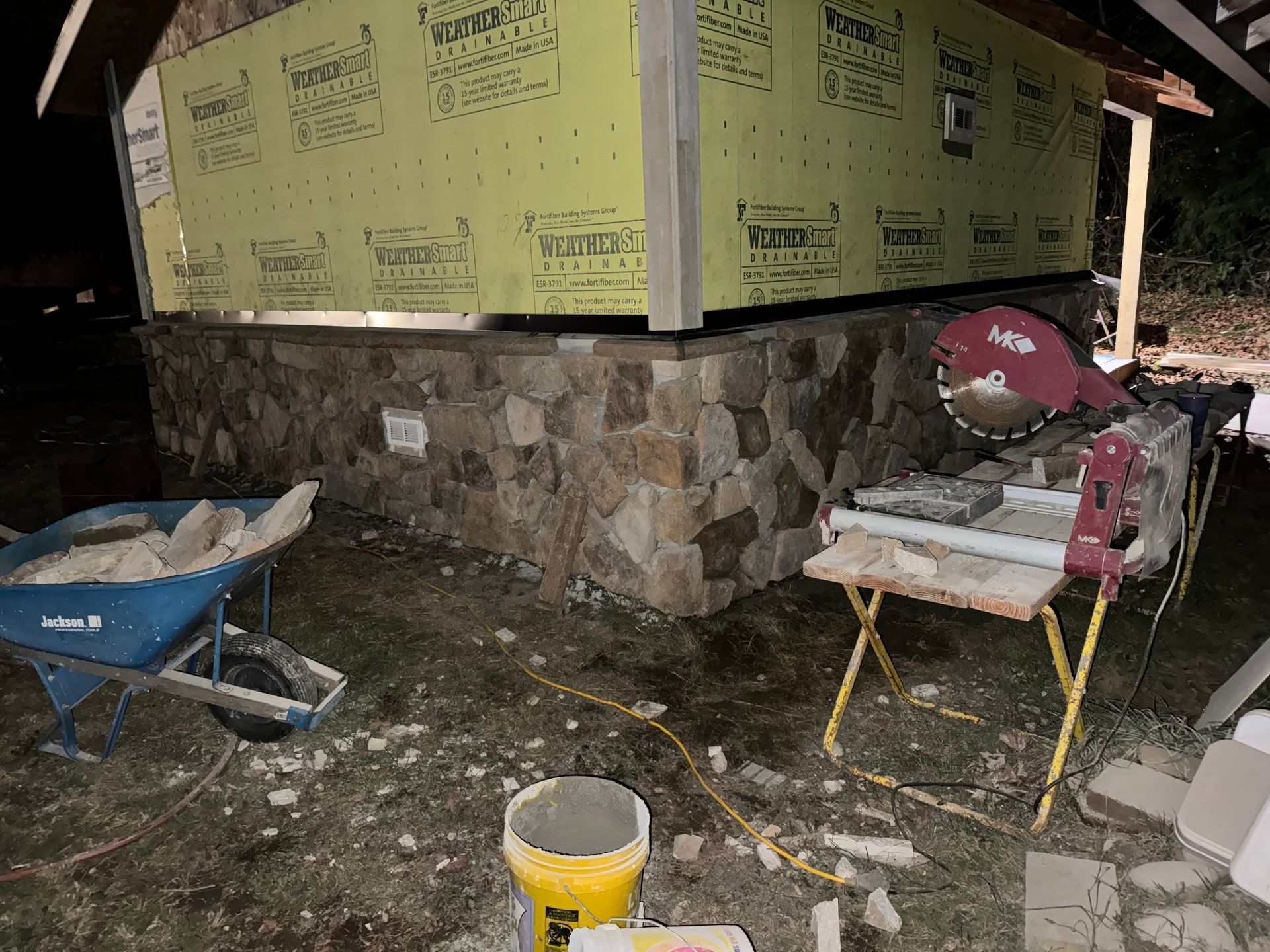 Stone facade under construction on a building. Saw and wheelbarrow nearby, work tools visible.