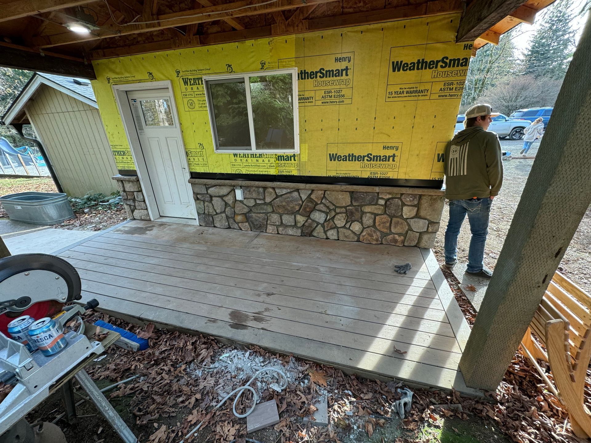 A partially built structure with stone base and yellow siding, a person standing nearby.