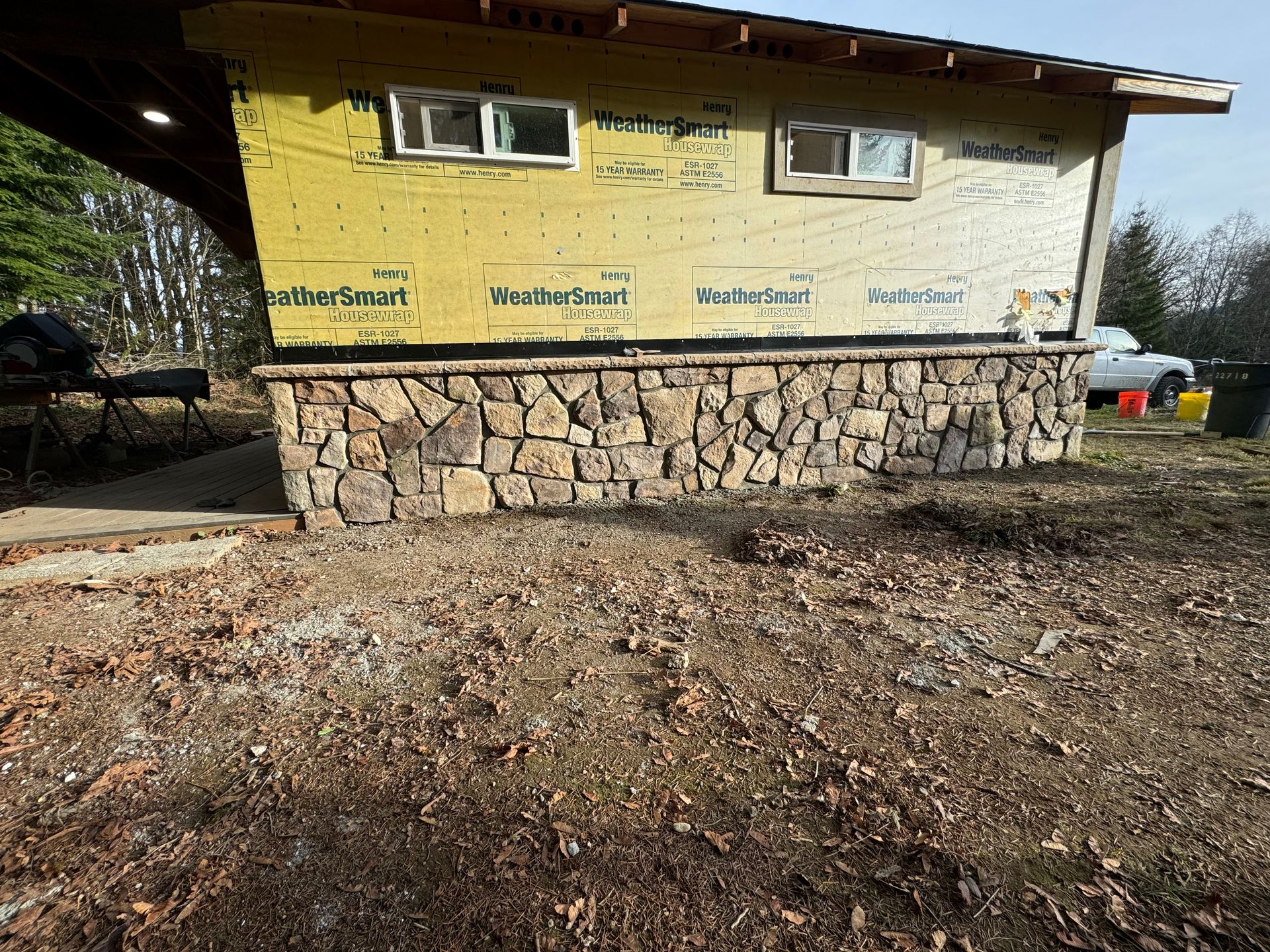 A small building with stone base and yellow siding, two windows, set in a yard.