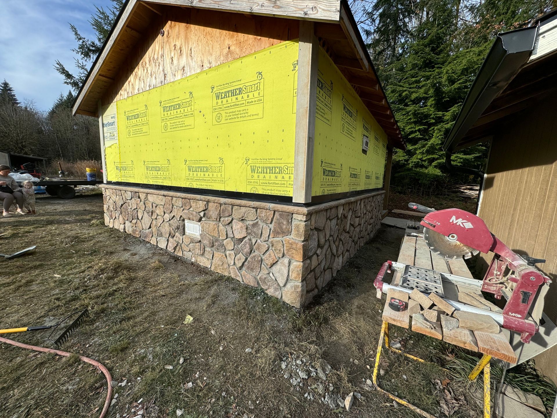 Stone veneer being installed on a building's base; construction in progress.