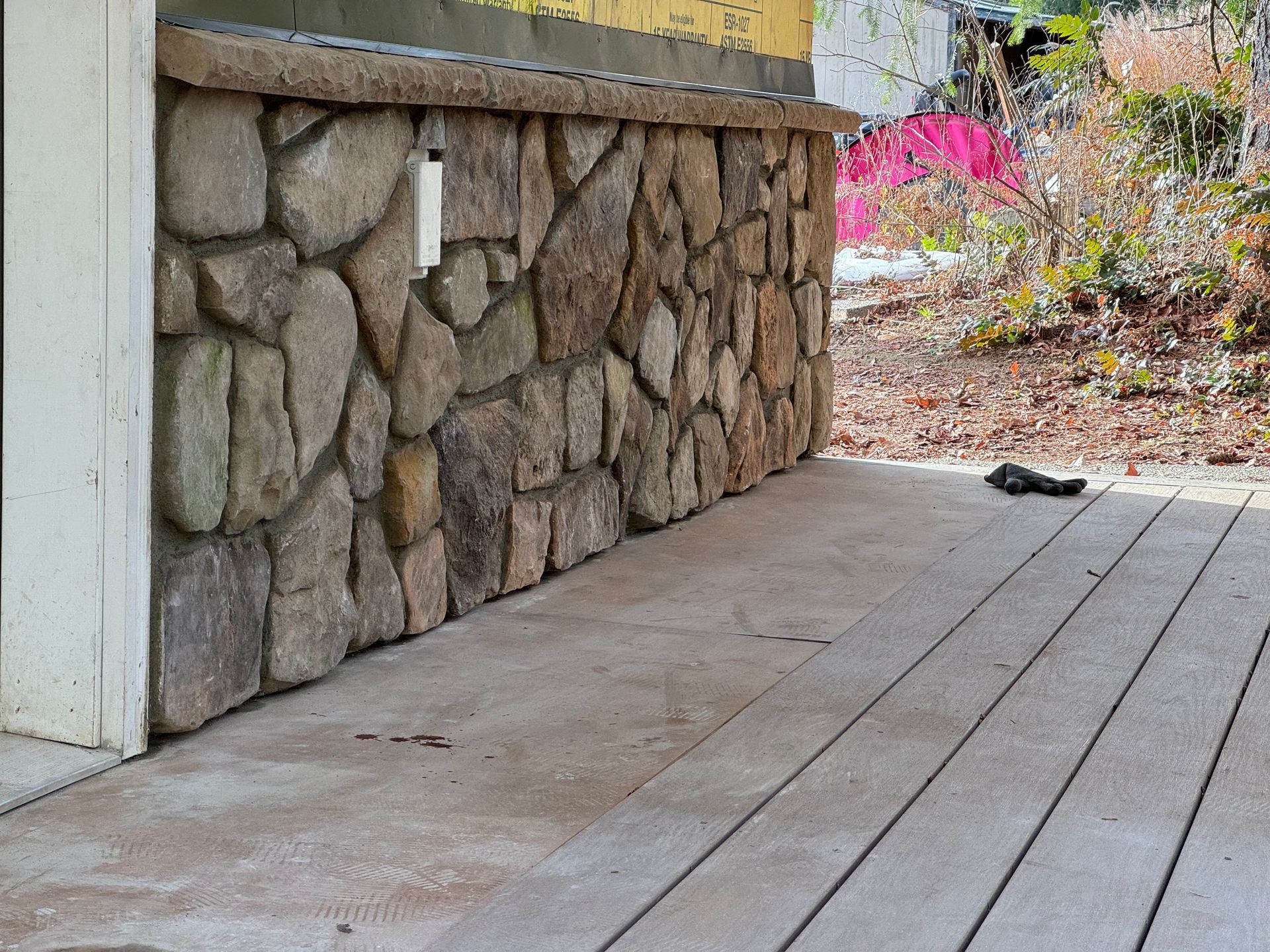 Stone wall on a building's exterior with a gray wooden deck in front.