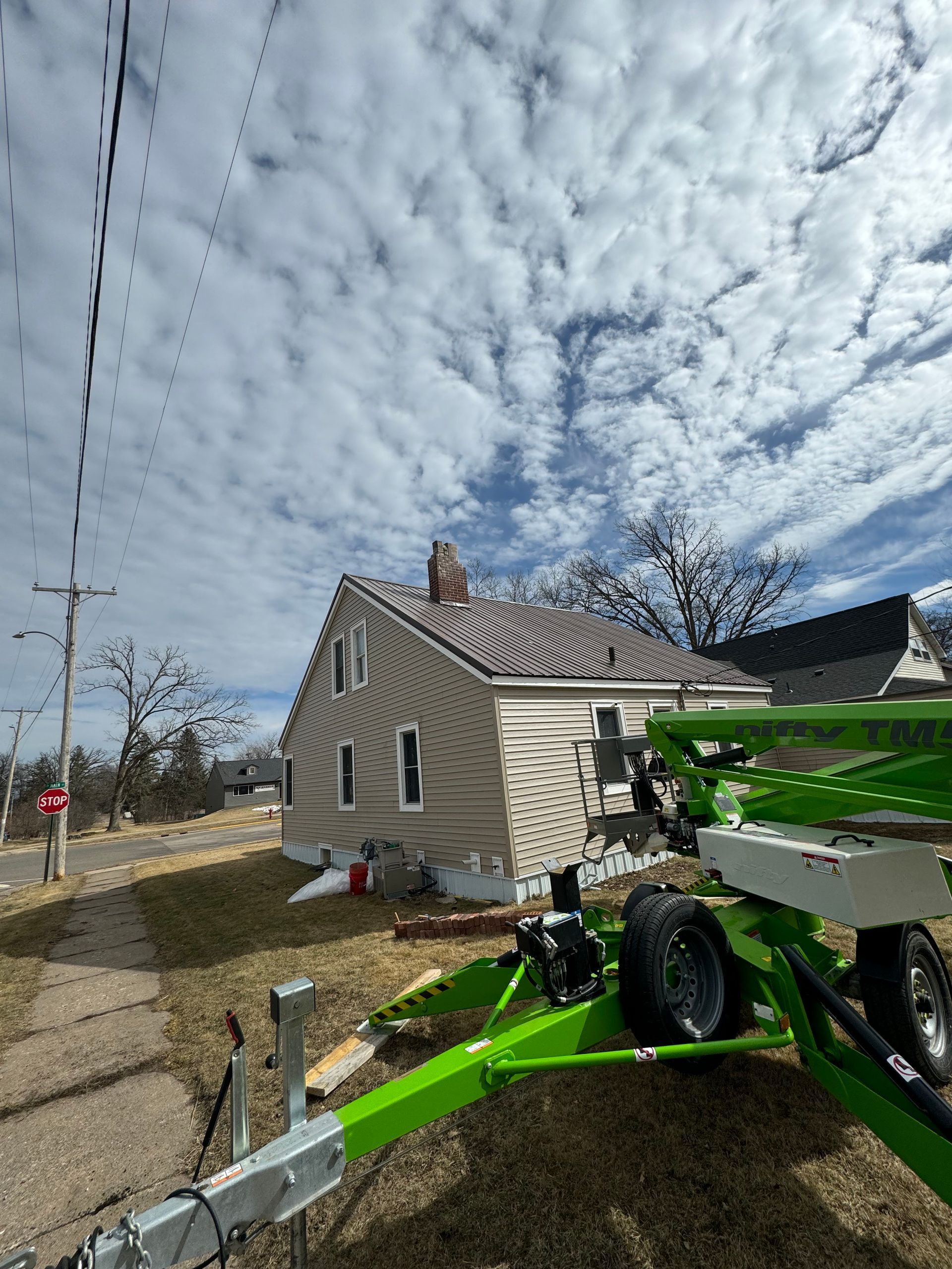 House with brown roof and gray siding on a cloudy day. Green equipment in foreground.