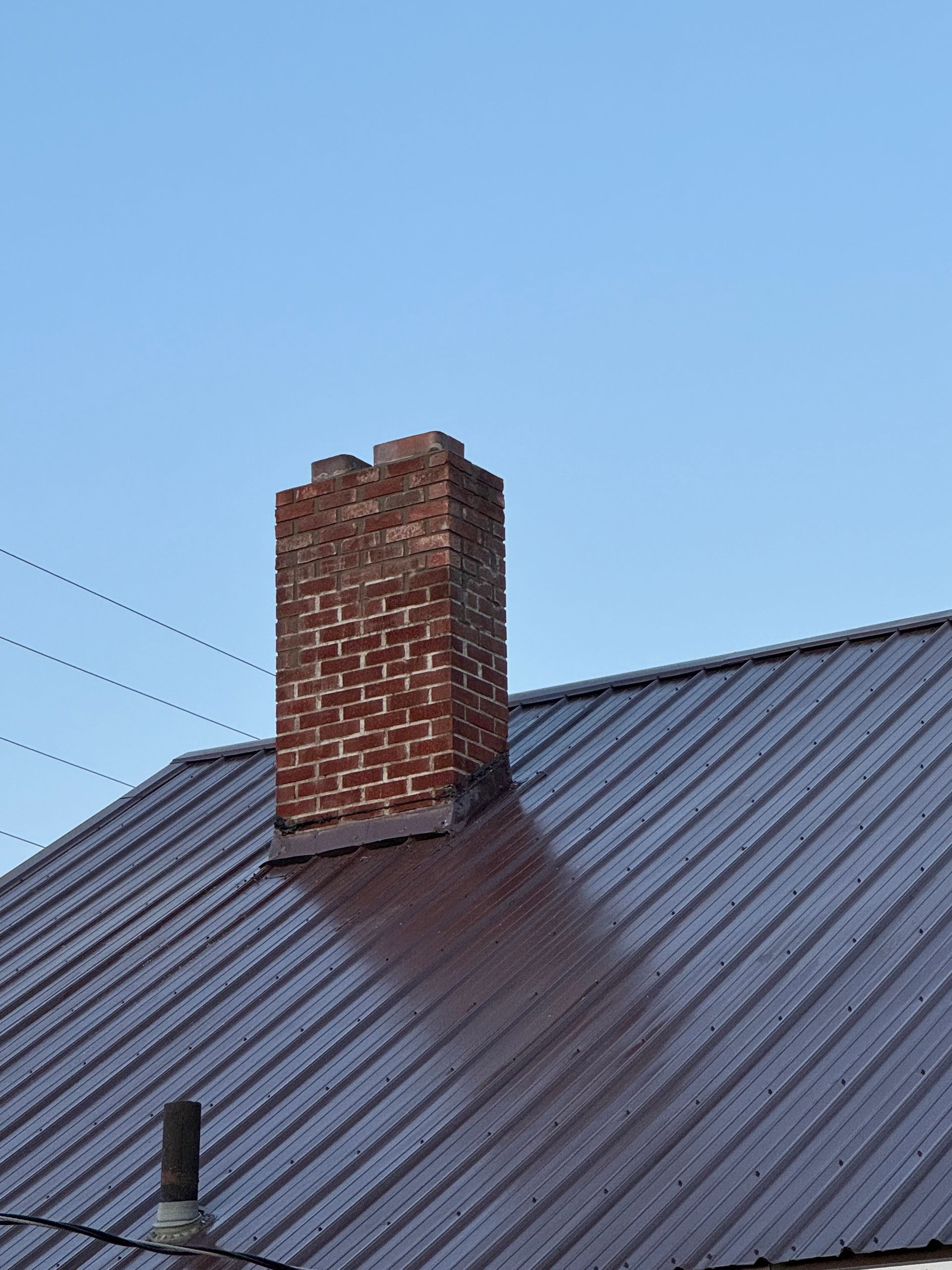 Brick chimney on a metal roof, casting a shadow against a blue sky.