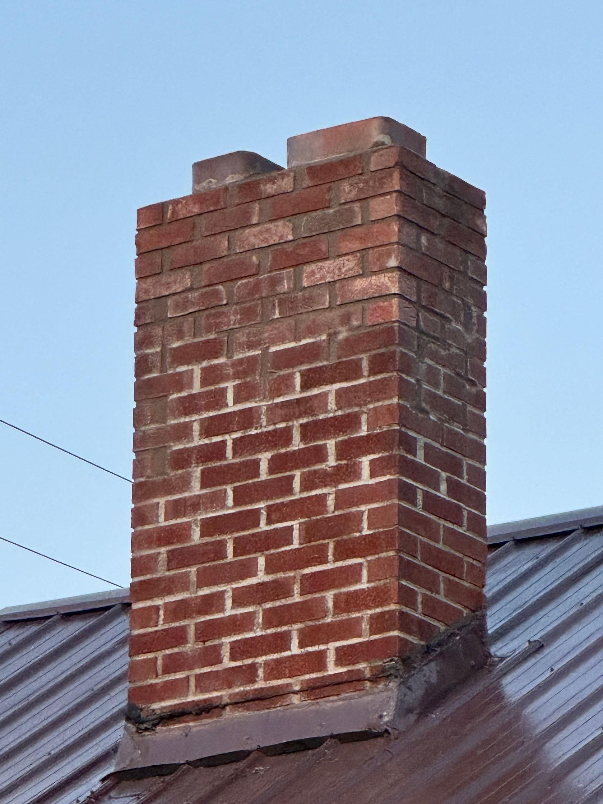 Brick chimney on a metal roof against a blue sky.