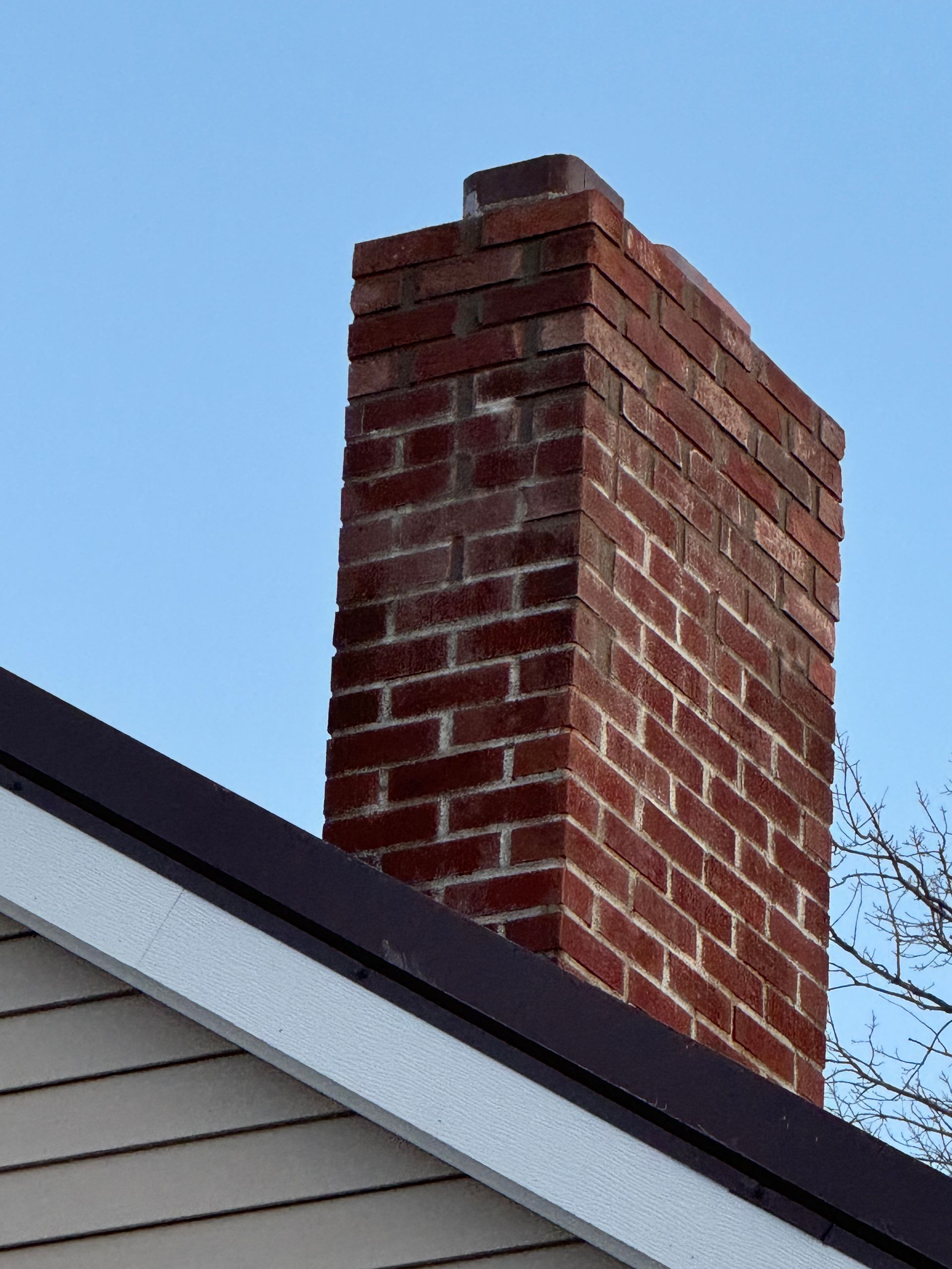 Brick chimney on a house roof against a blue sky.