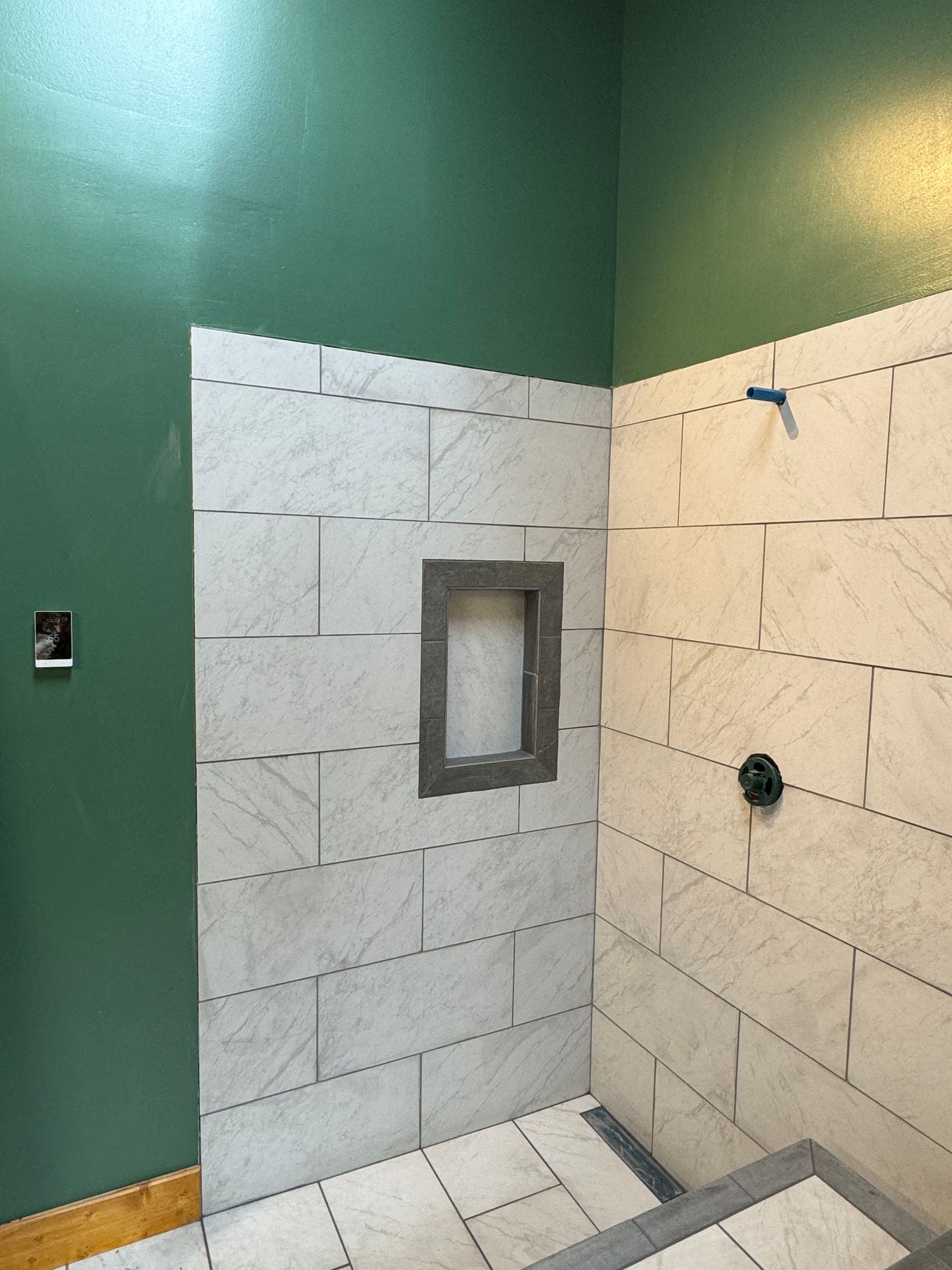 Bathroom shower with partially tiled walls, a built-in shelf, and green paint on the adjacent wall.