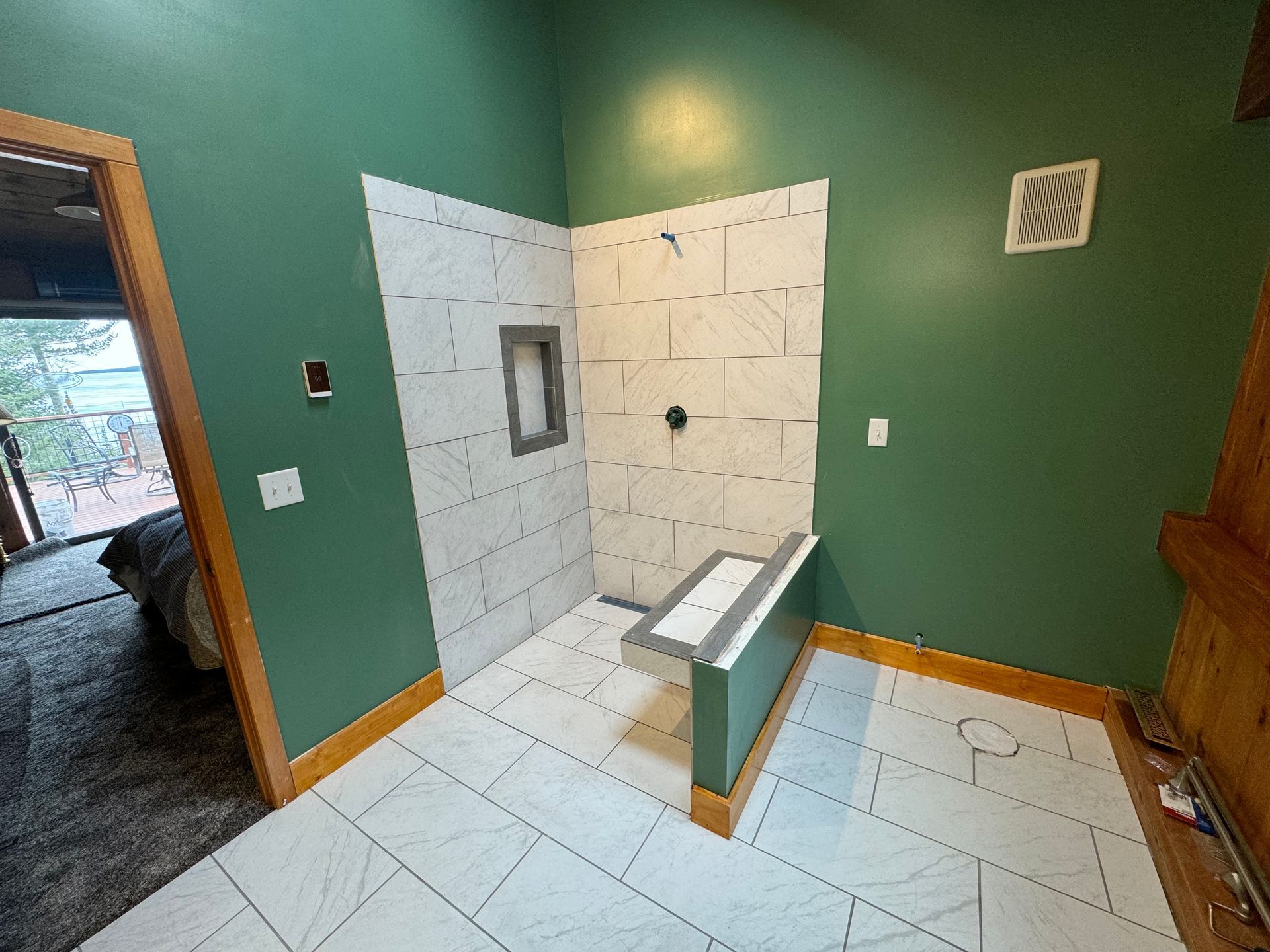Bathroom with white tiled shower, green walls, and a built-in bench.