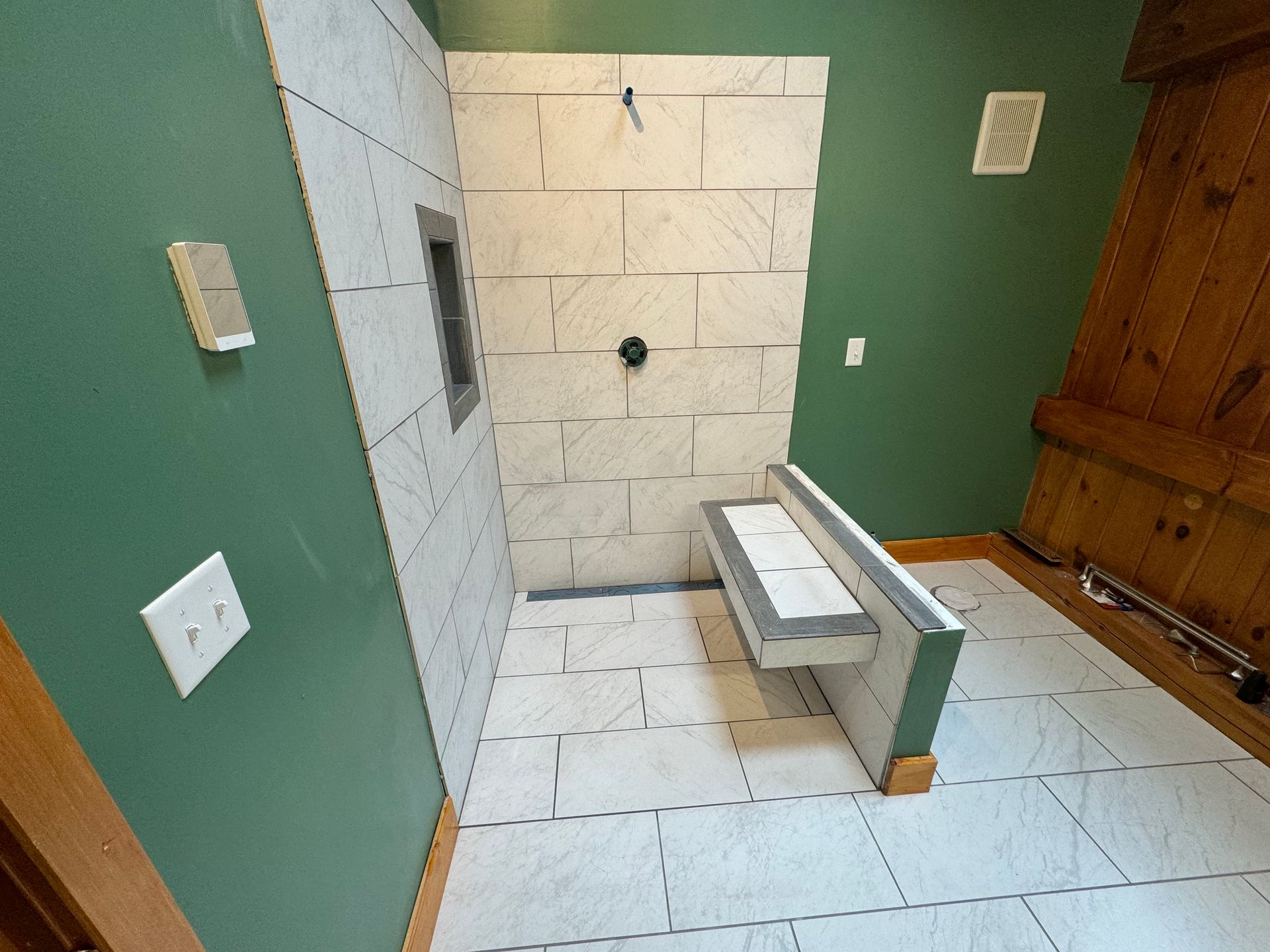 Bathroom with tiled shower, built-in bench, green walls, and wood paneling. Partially completed renovation.