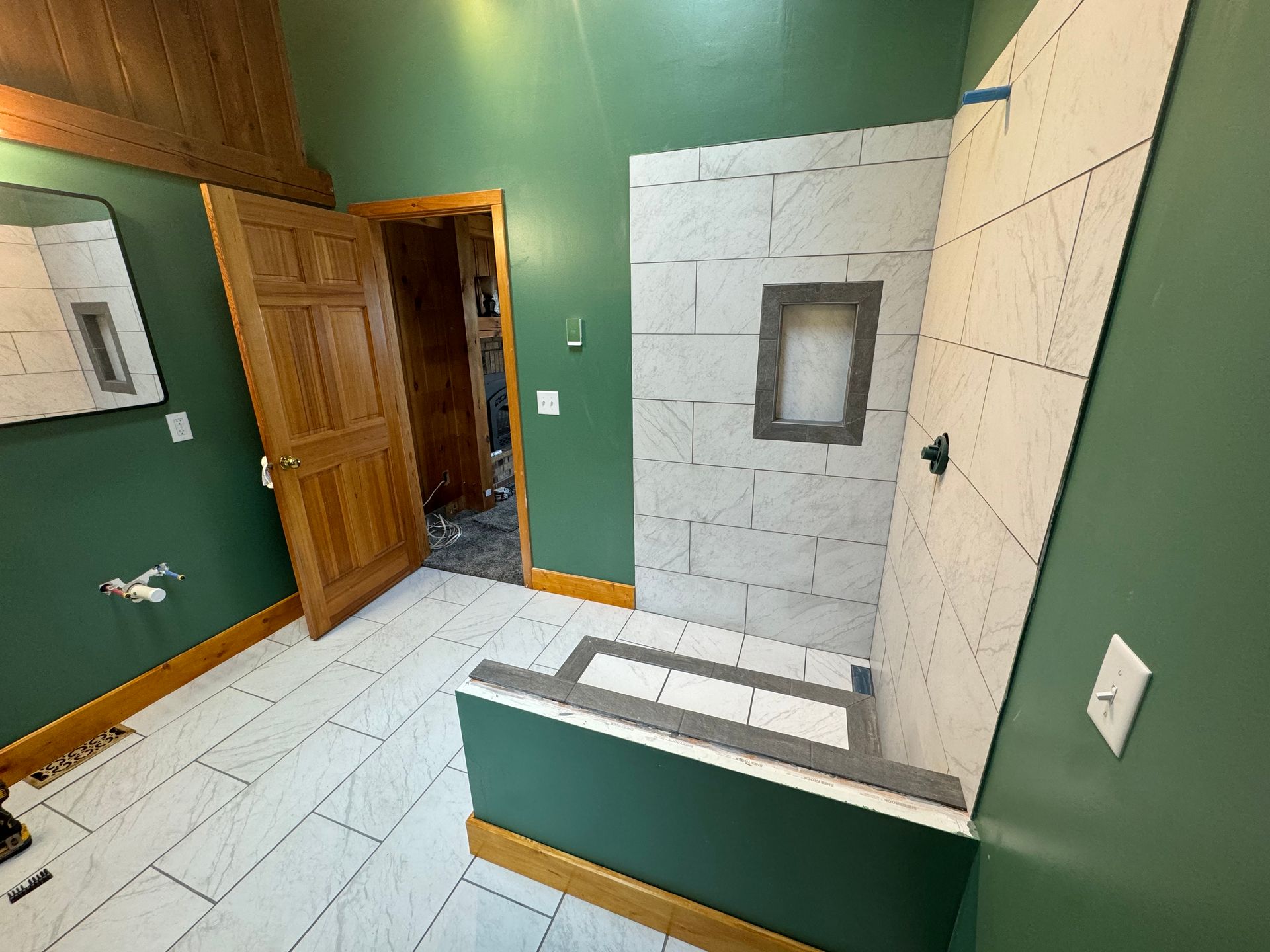Bathroom renovation in progress: green walls, white tile, wooden door, shower area with installed tile.