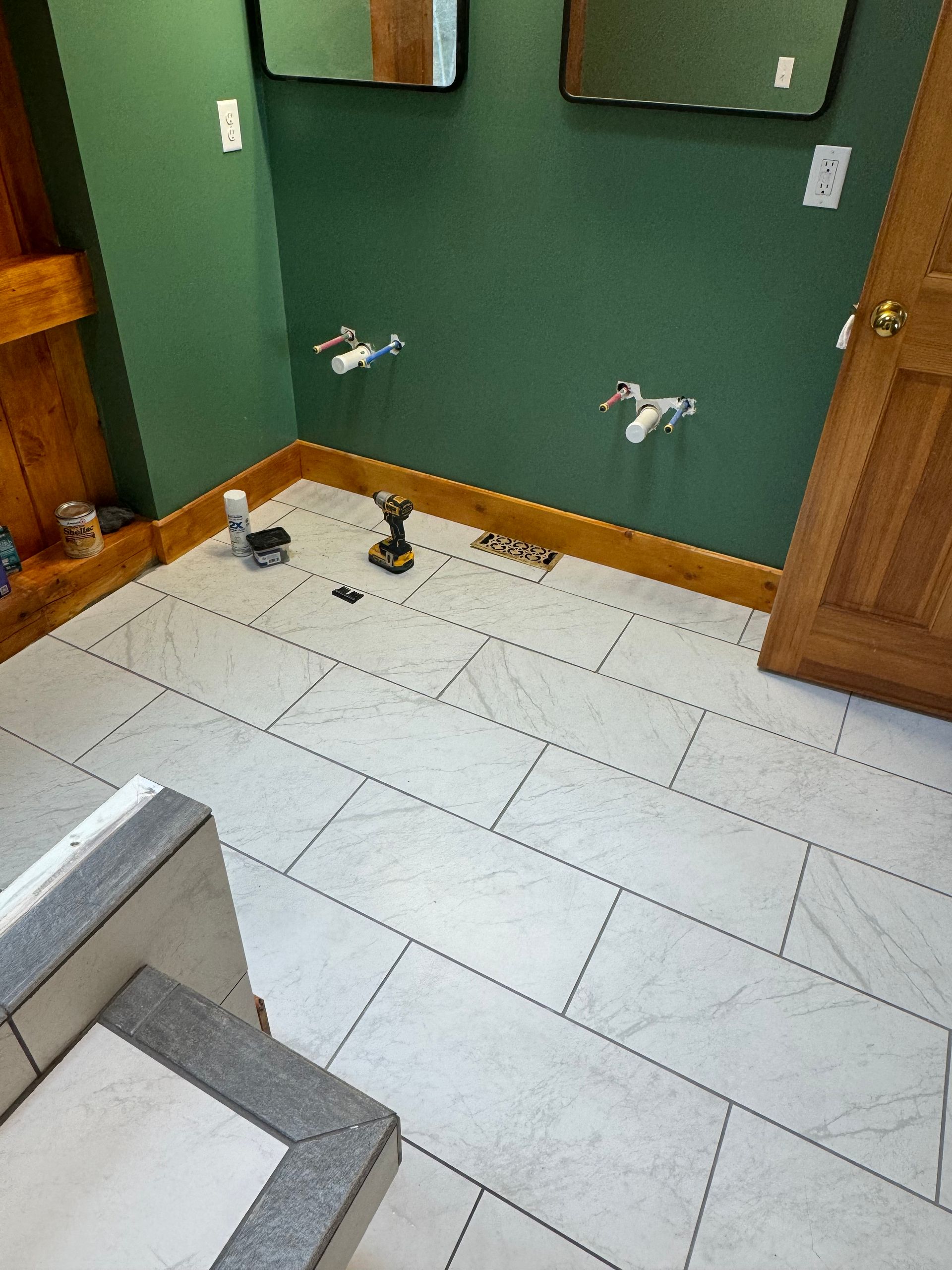 Bathroom with white tiled floor, green walls, wooden trim, mirrors, and plumbing fixtures.