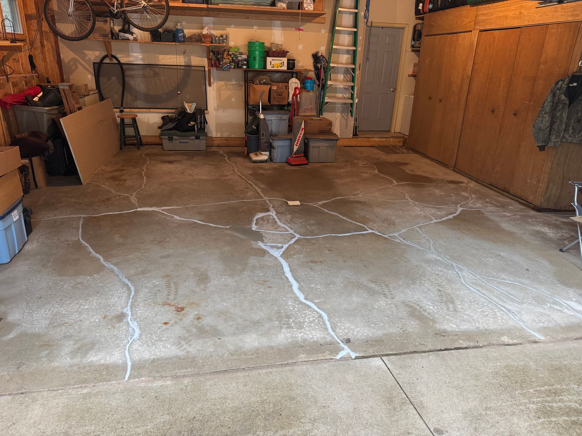 Garage floor with numerous white-filled cracks. Various tools, boxes, and a ladder are visible.