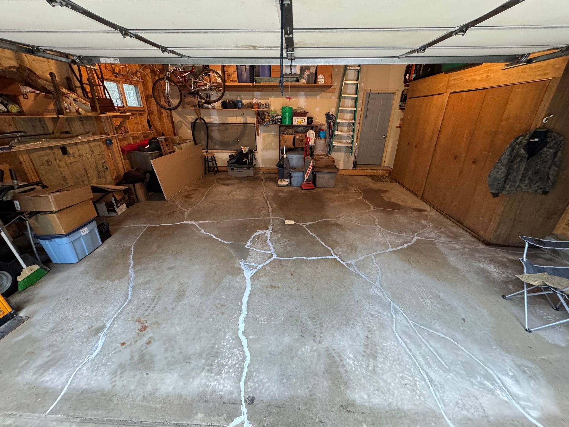 Cracked concrete garage floor; white sealant fills cracks. Garage interior with cluttered storage and open door.