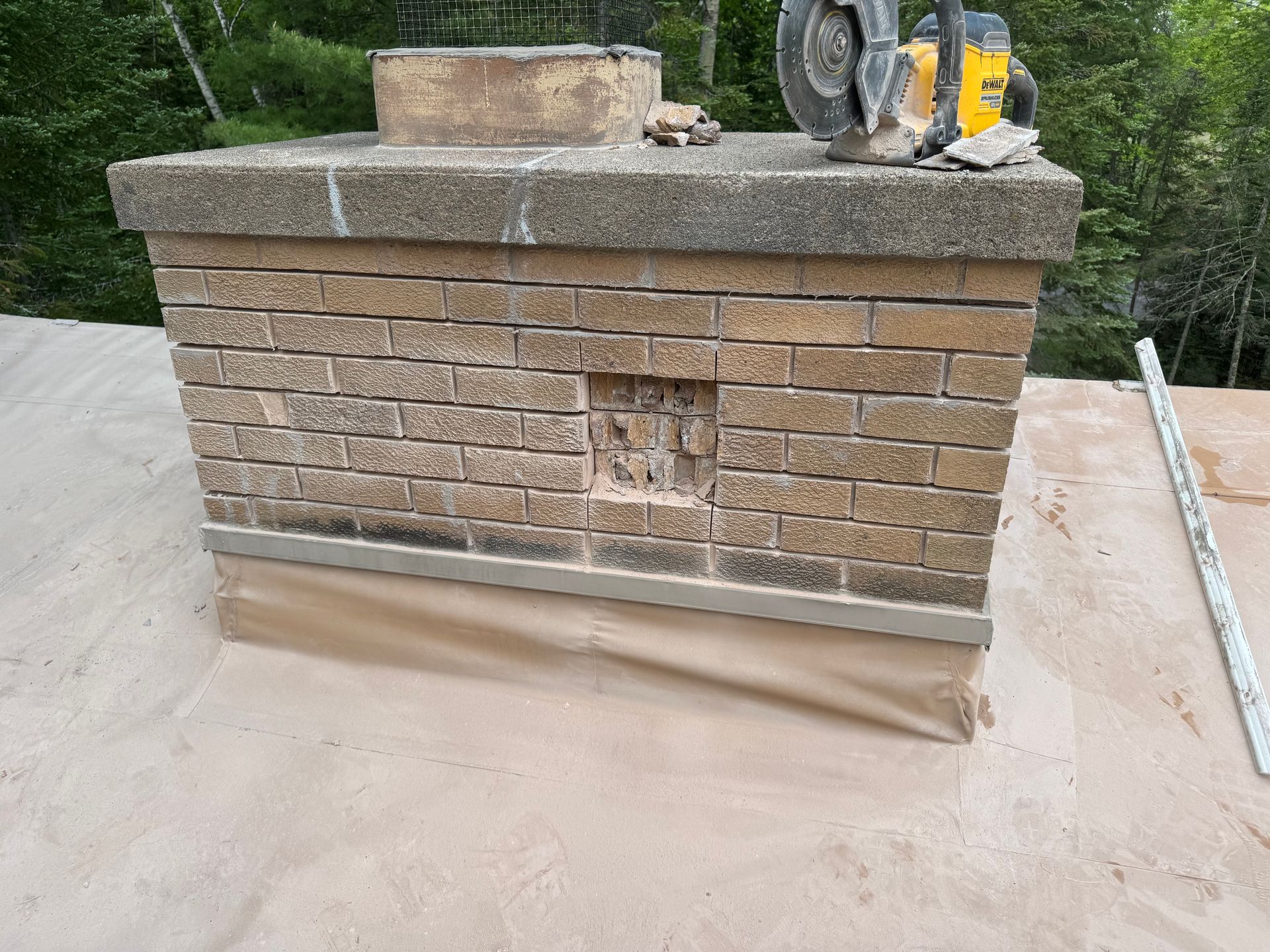 Brick chimney with a hole, topped with stone, on a roof. A circular saw sits on top.