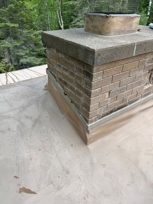 Chimney on a flat roof, made of brick and concrete. Brown and tan colors.