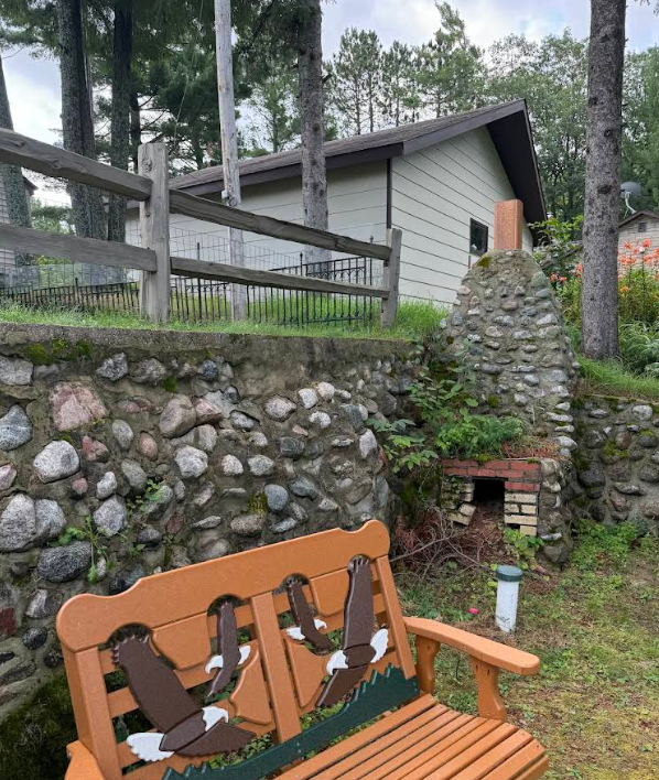 Wooden bench with eagle designs, stone wall, and a small building with chimney.